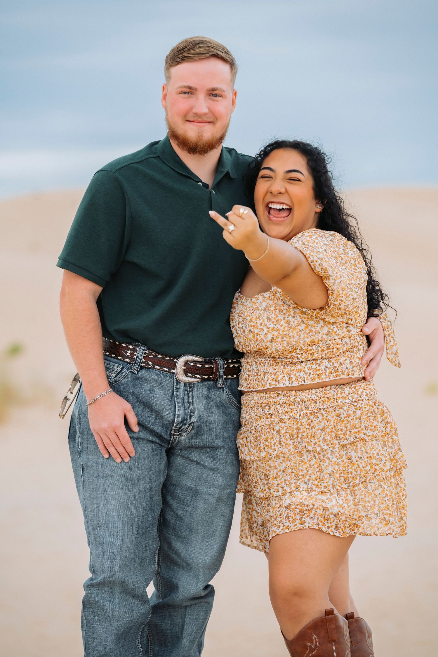 A couple poses playfully in a desert setting wearing casual attire and sharing joyful moments together.