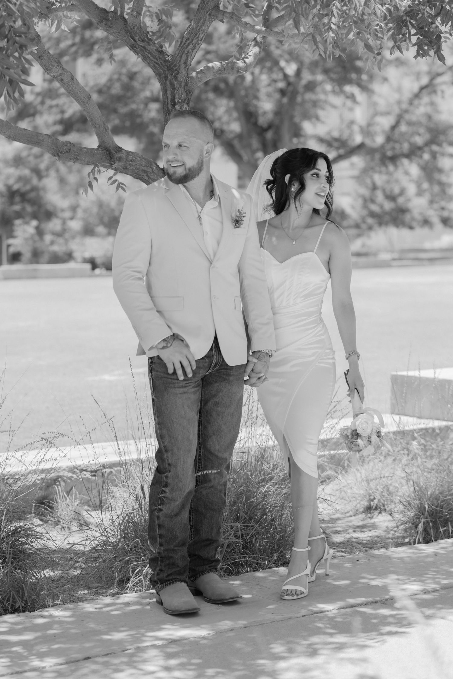 A romantic black and white photo of a couple in formal attire posing outdoors against a scenic natural backdrop.