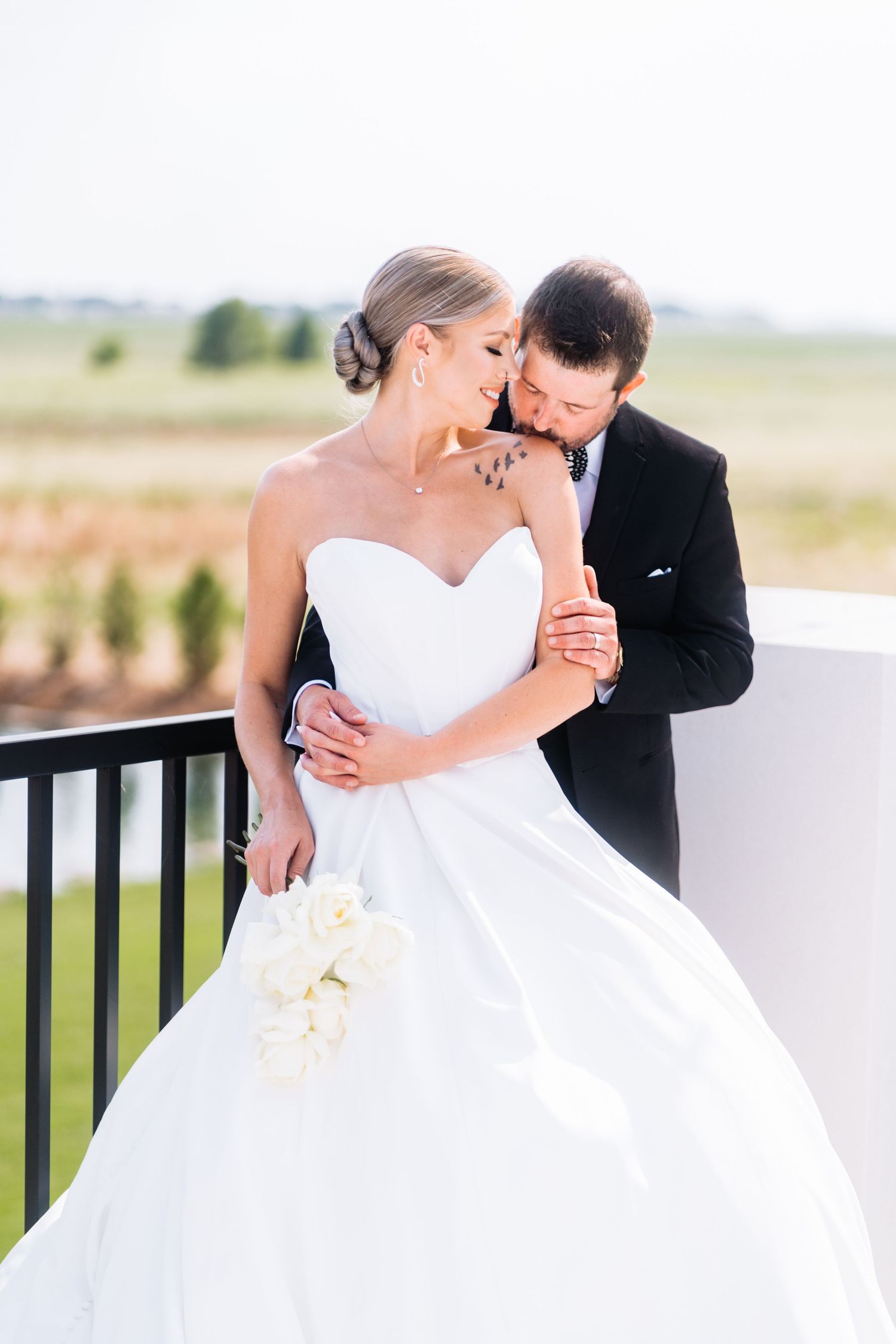 An intimate wedding portrait showing a tender embrace on a sunlit balcony.