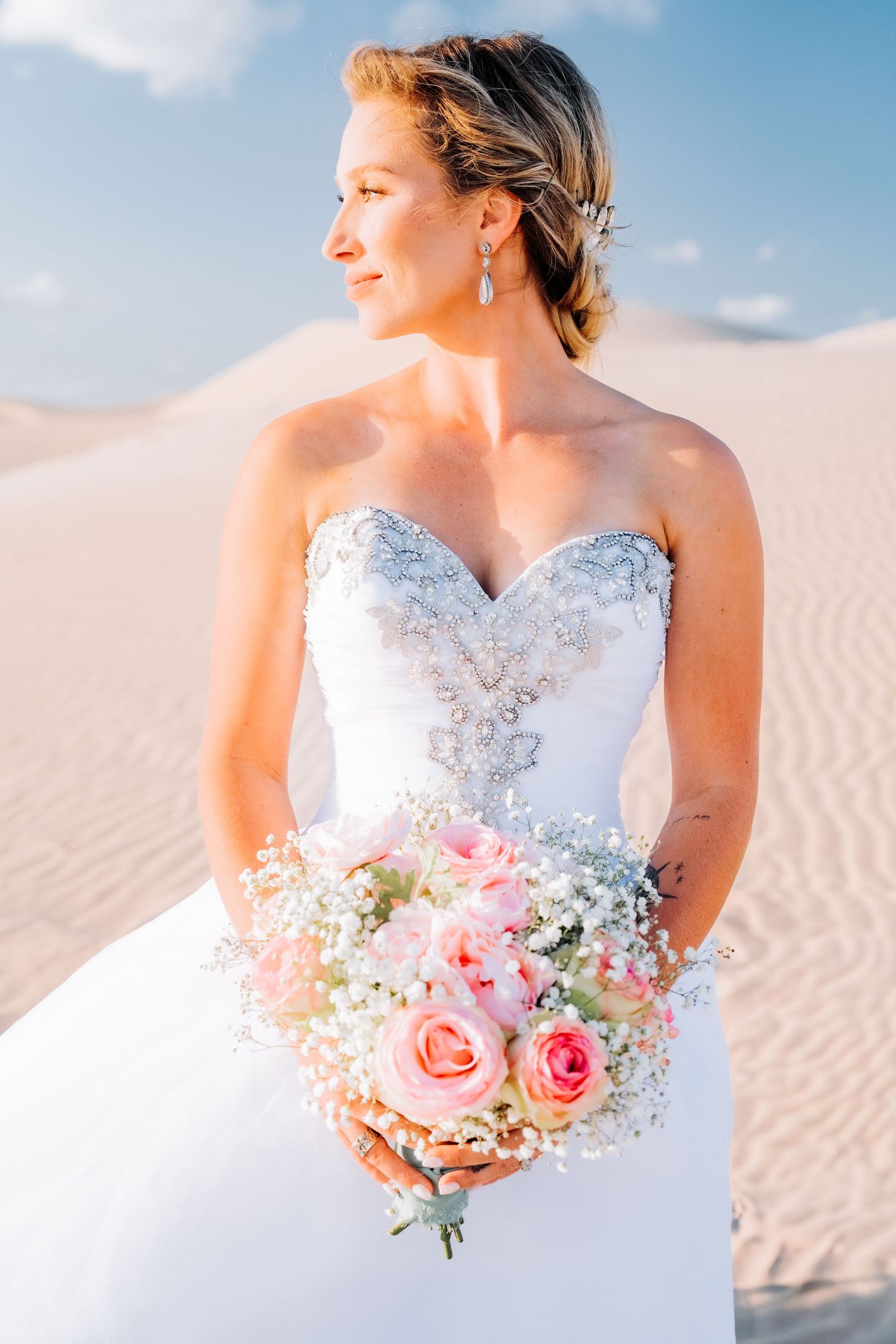 Side profile of bride with floral bouquet against desert sand dunes.