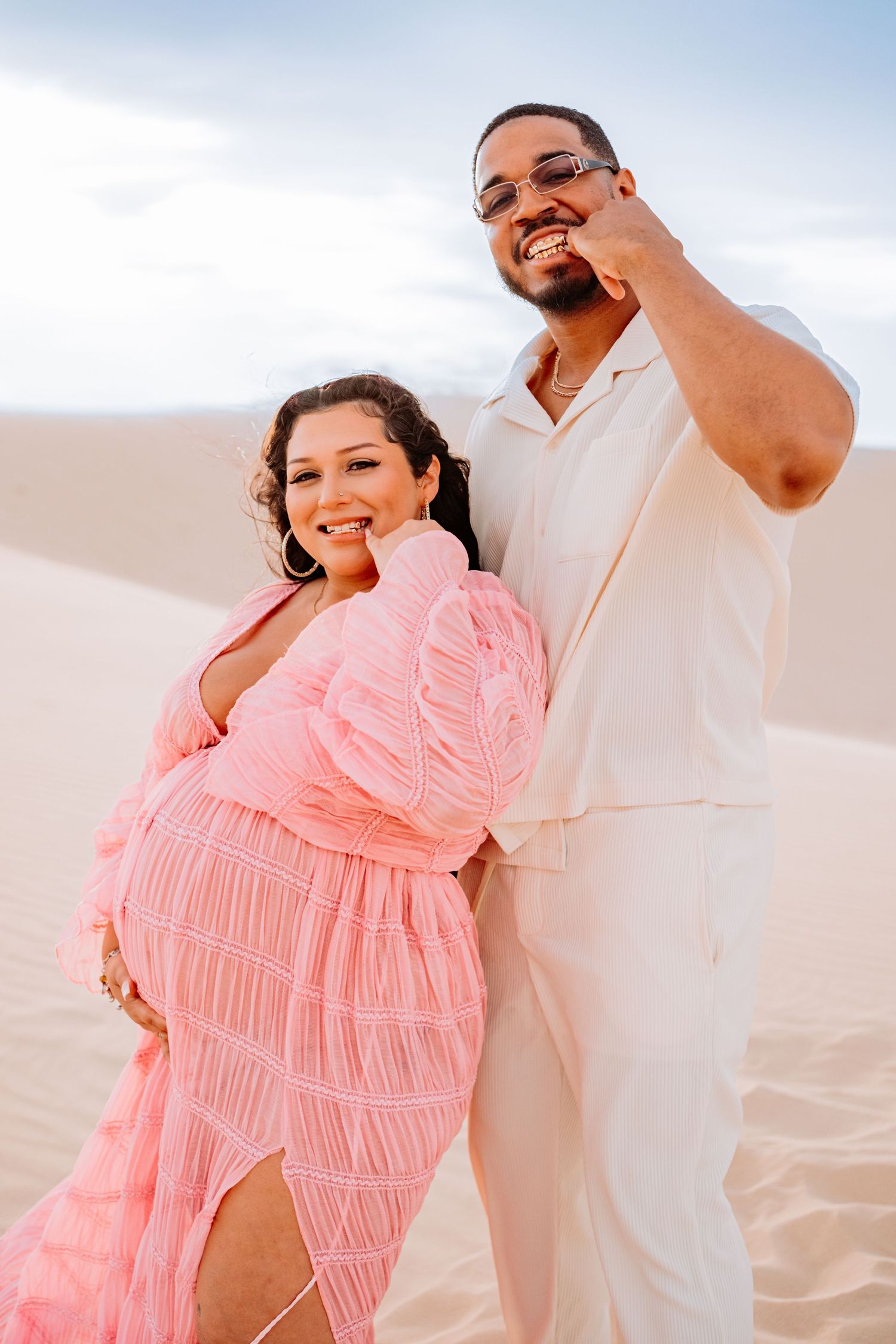 Happy couple poses together in desert wearing coordinating pink dress and white outfit.