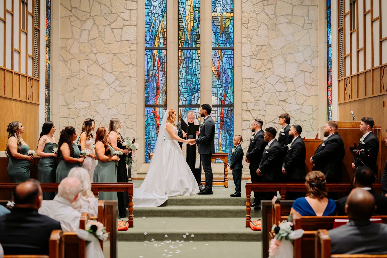 Wedding ceremony taking place in a church sanctuary with beautiful blue stained glass windows and stone walls.