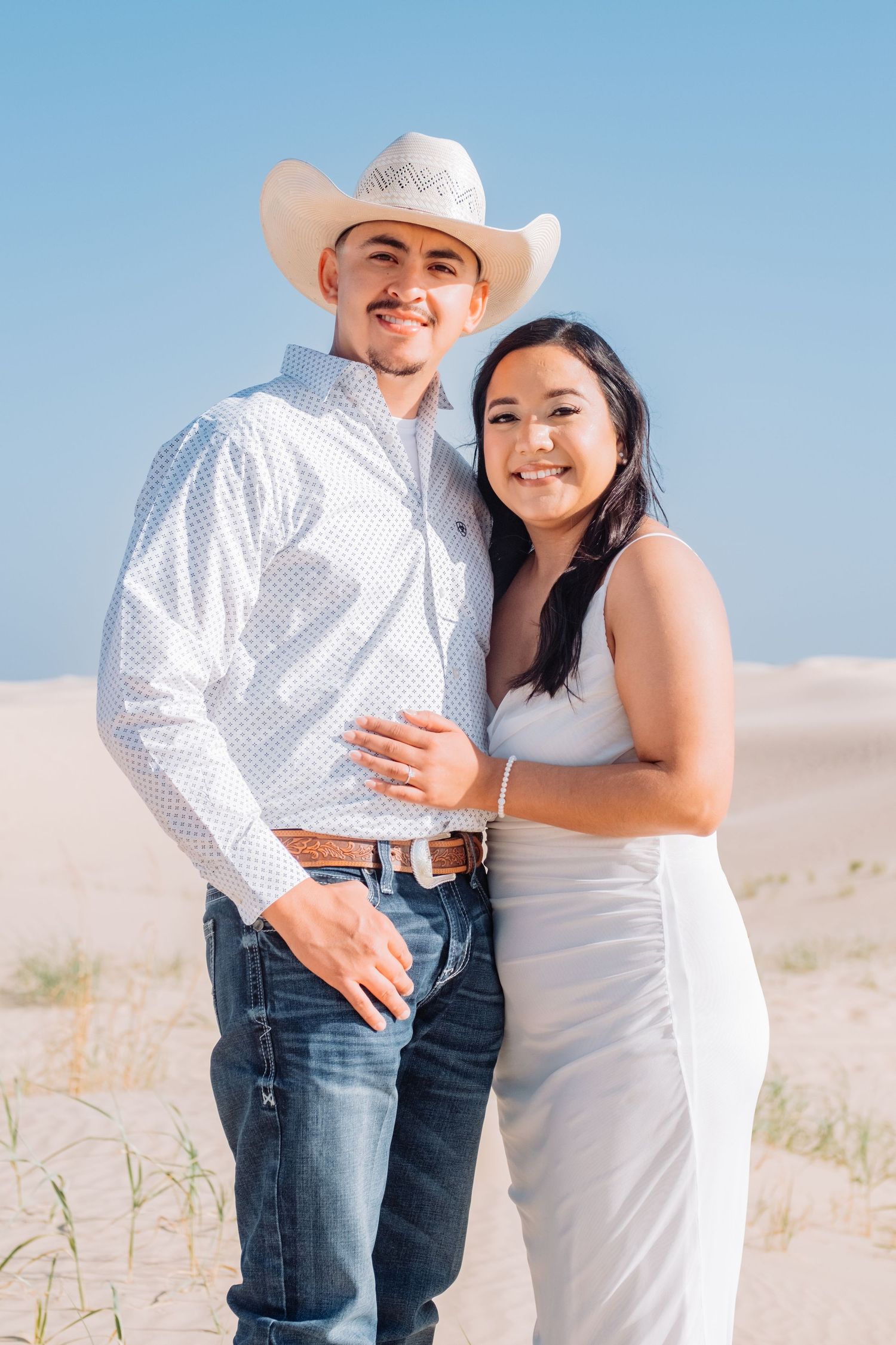Couple in western wear smiling together against desert landscape.