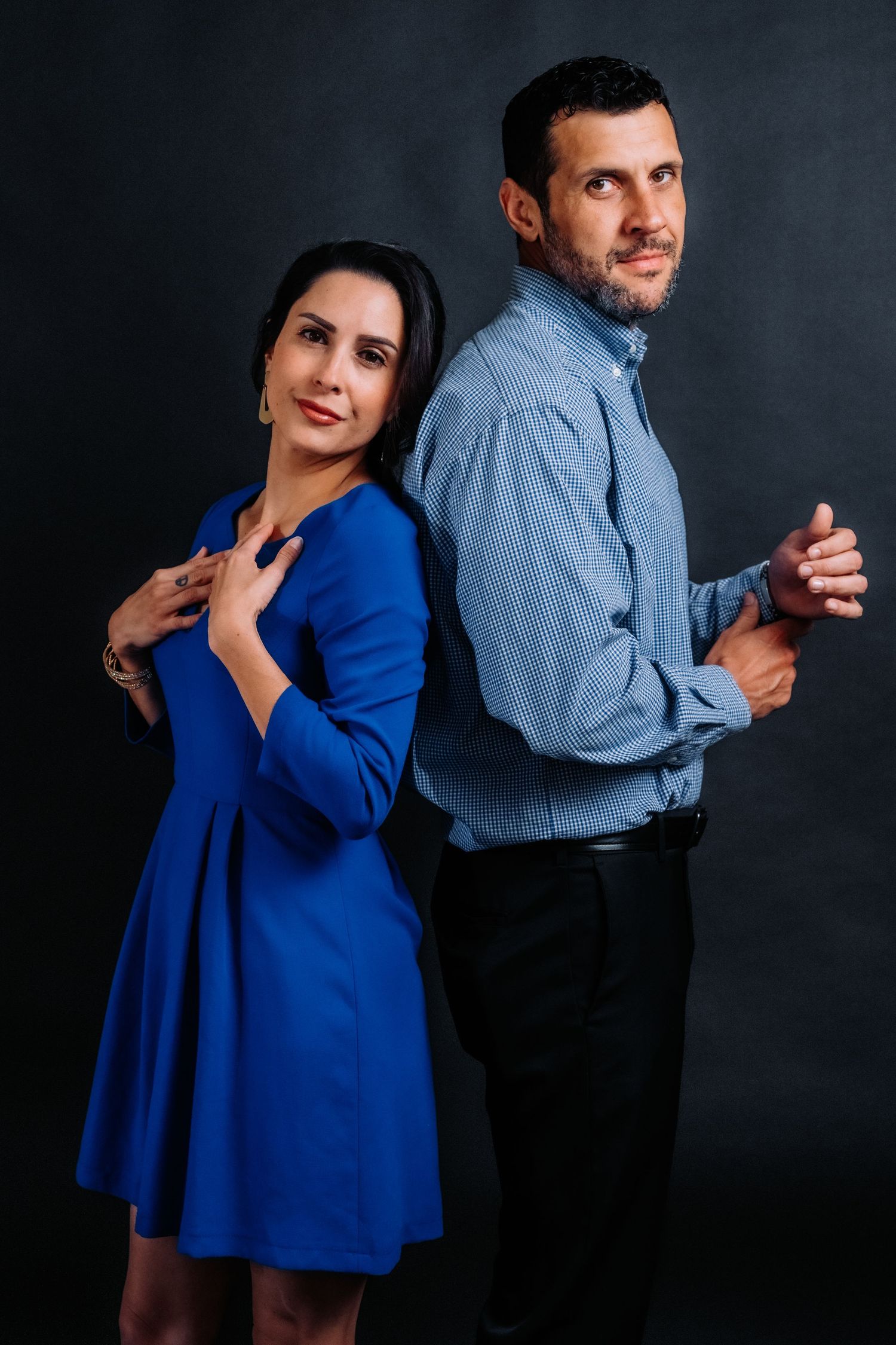 Studio portrait of couple posing back-to-back, woman in blue dress and man in denim shirt.