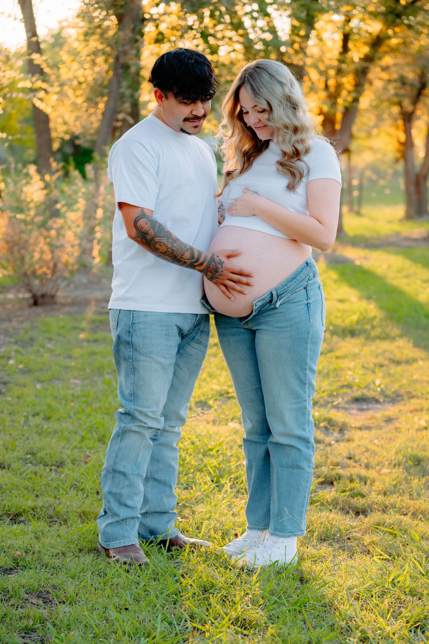 Intimate maternity photos of a couple against sun-dappled trees.