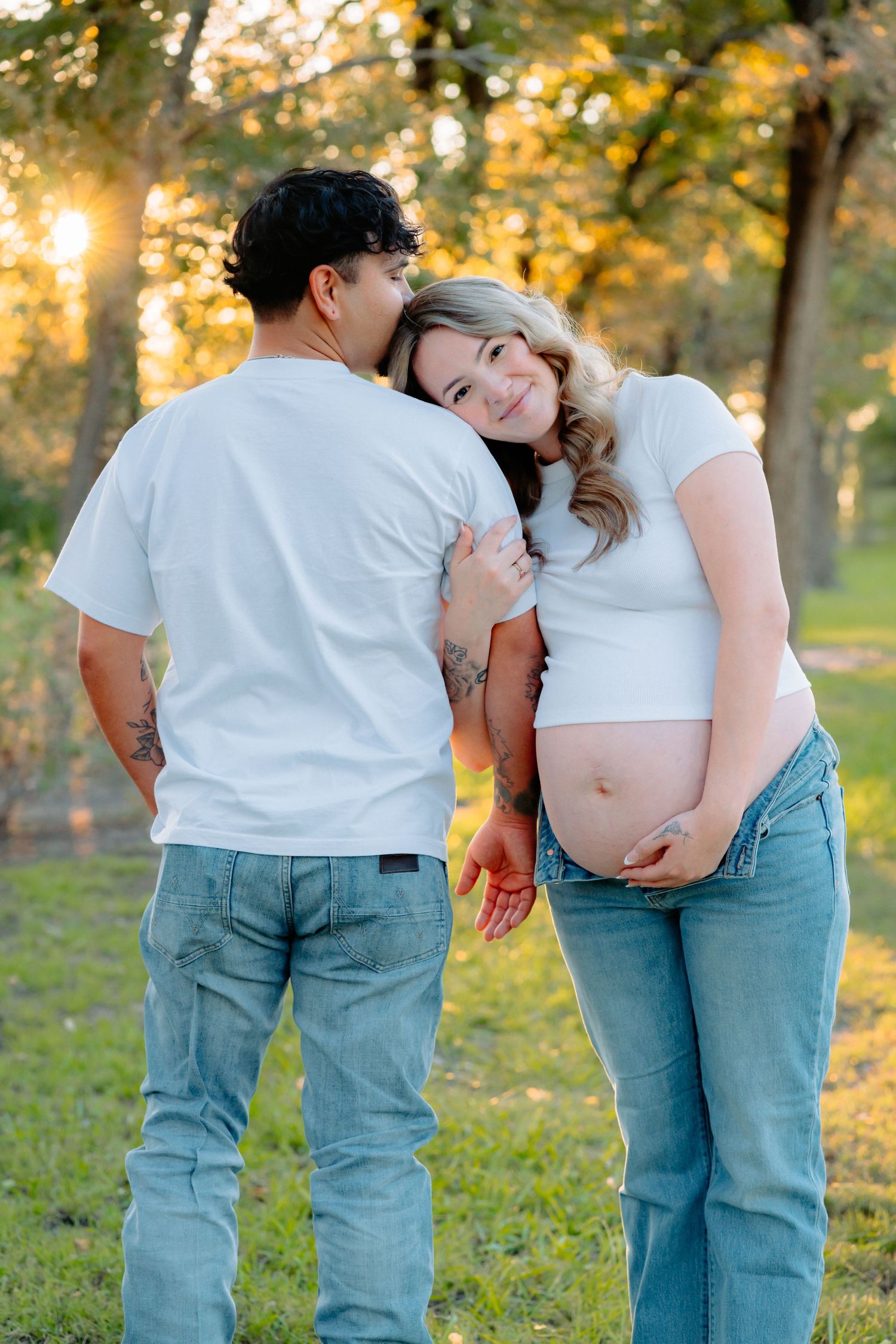 Casual couple shares tender moments in a park with warm sunset light filtering through trees.