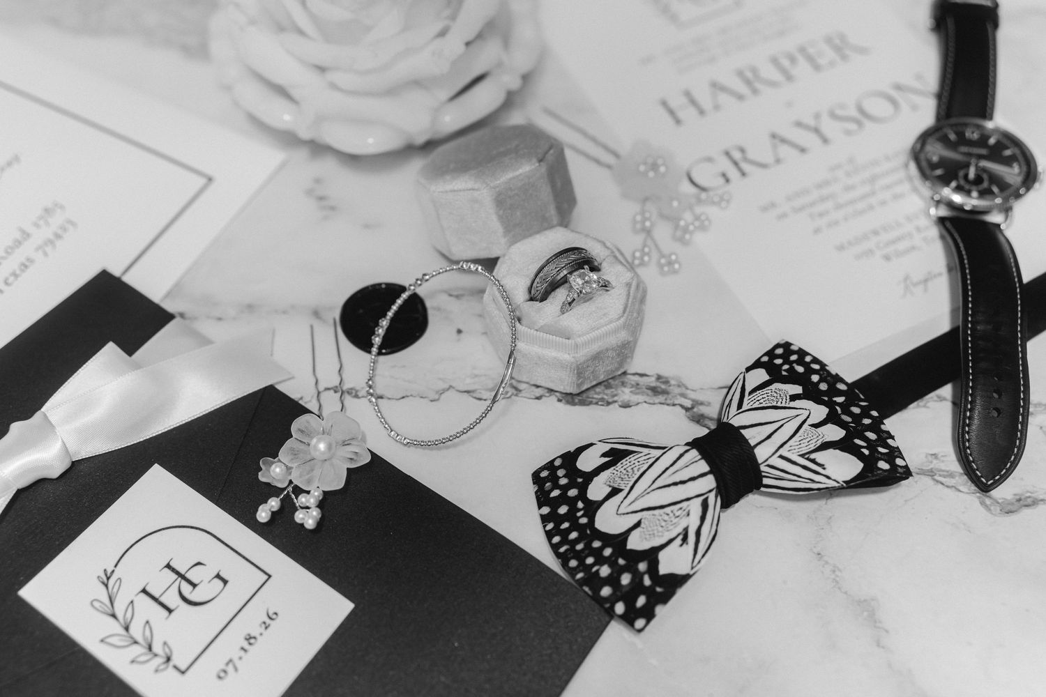 Black and white flat lay of wedding accessories including a bowtie and sunglasses.