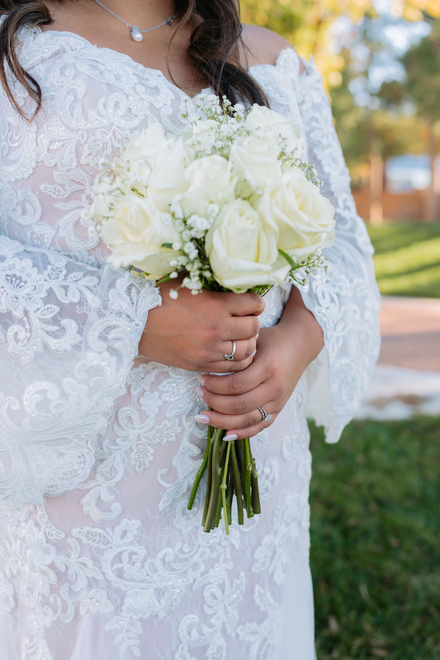 Close-up of bridal bouquet with white roses and lace dress detail.