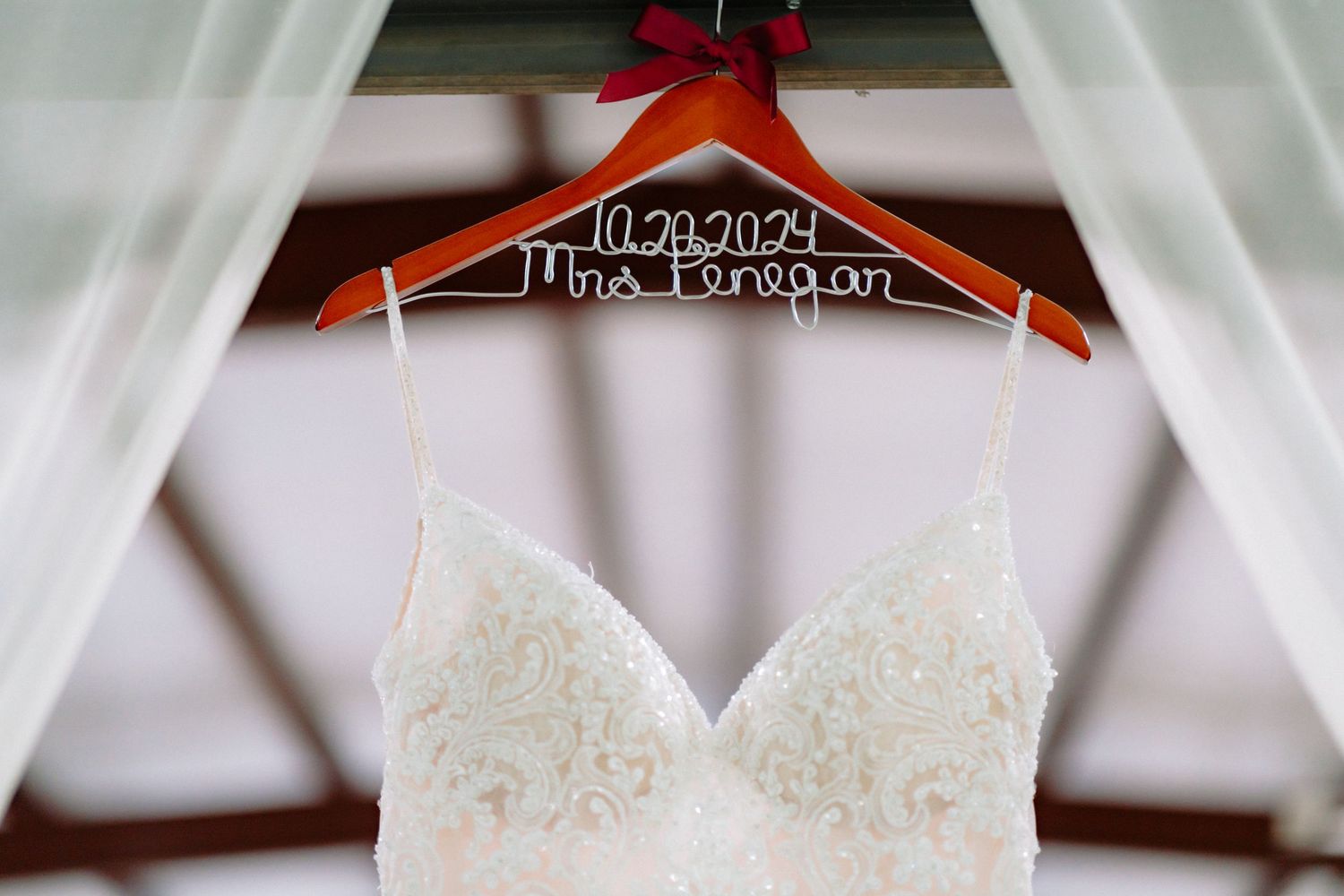 Wedding dress hangs on personalized wood hanger with lace bodice detail.