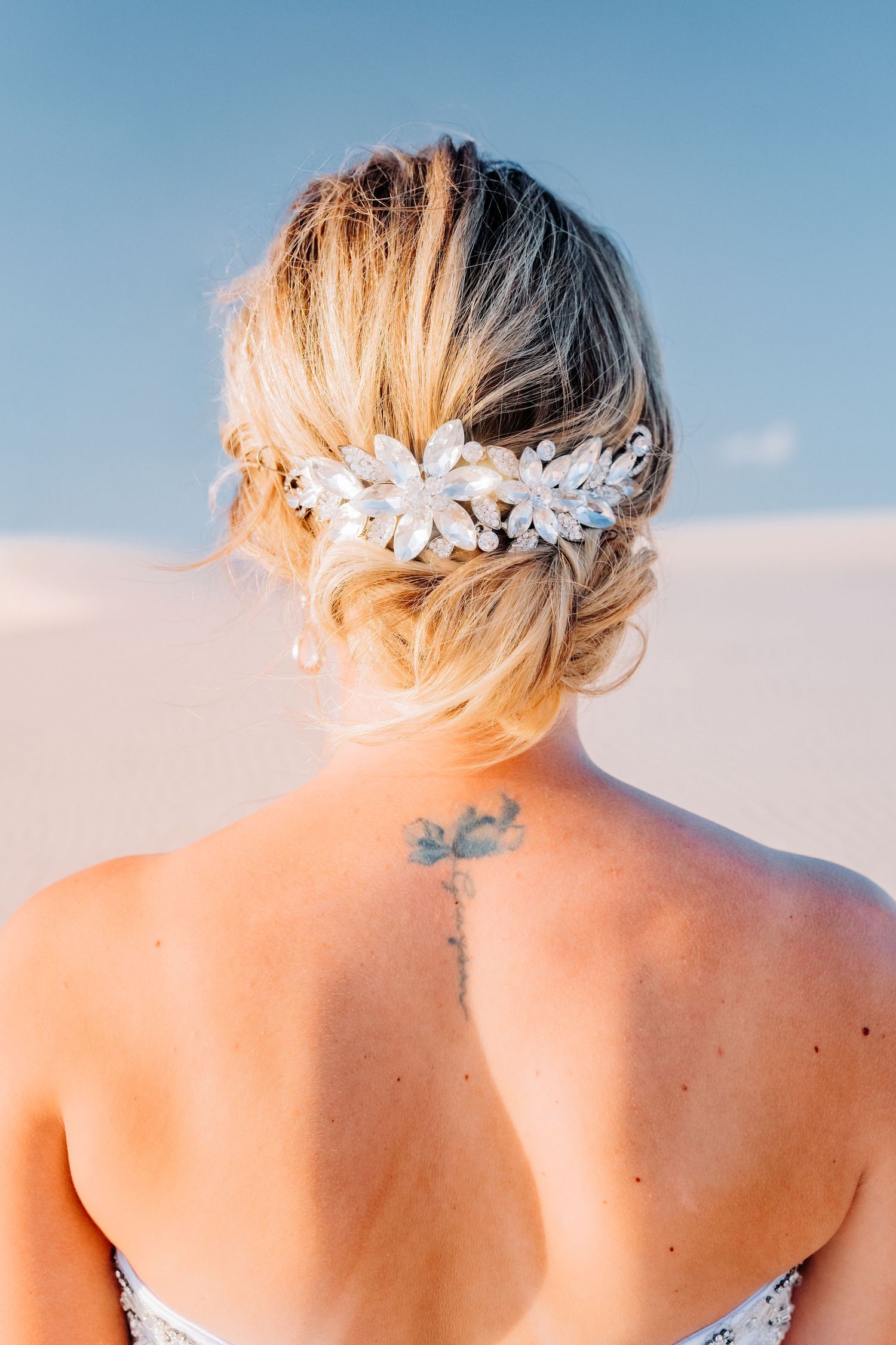 Back view showing bridal hair accessory and small tattoo against desert backdrop.