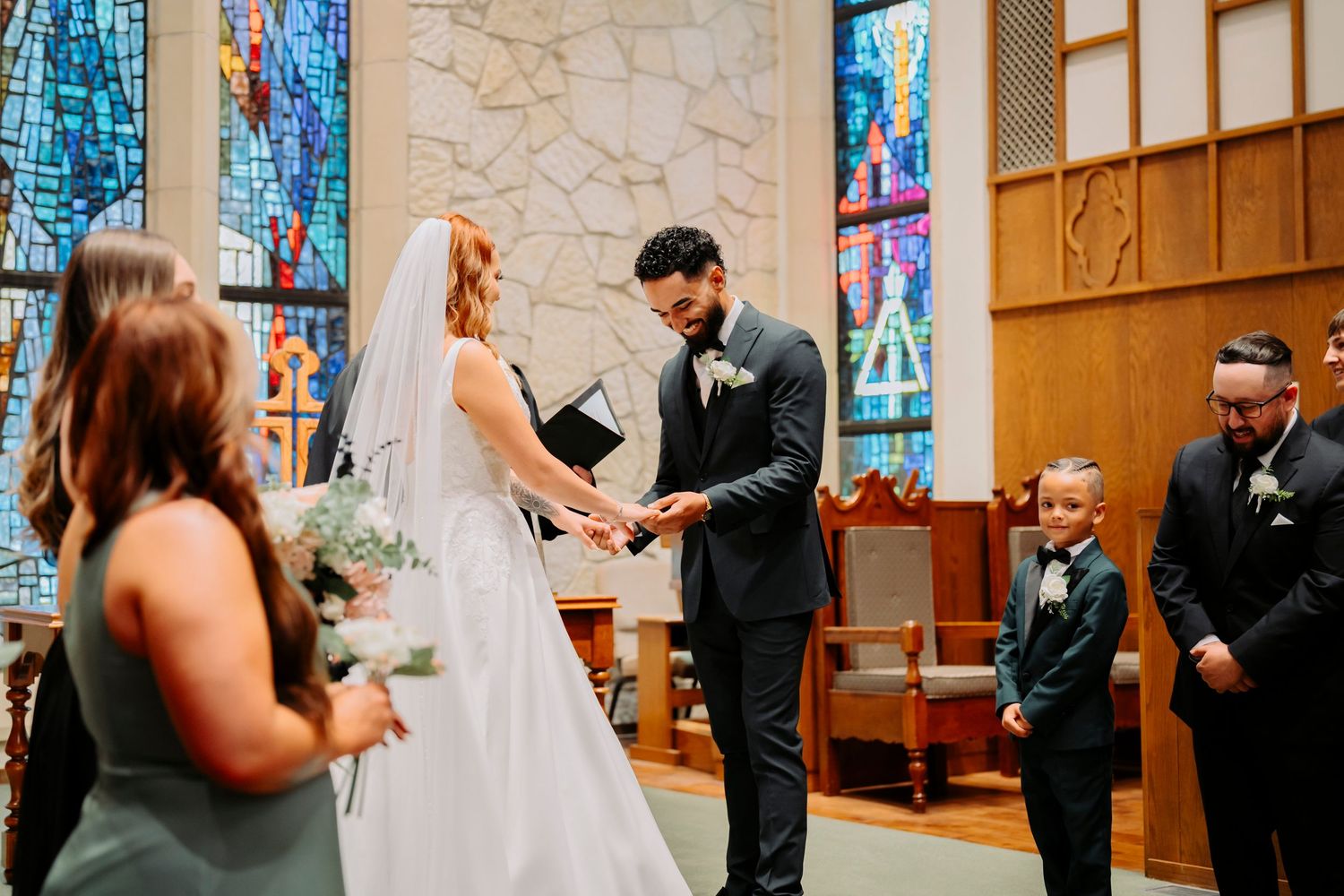 Intimate wedding ceremony moment in front of colorful stained glass windows in church sanctuary.