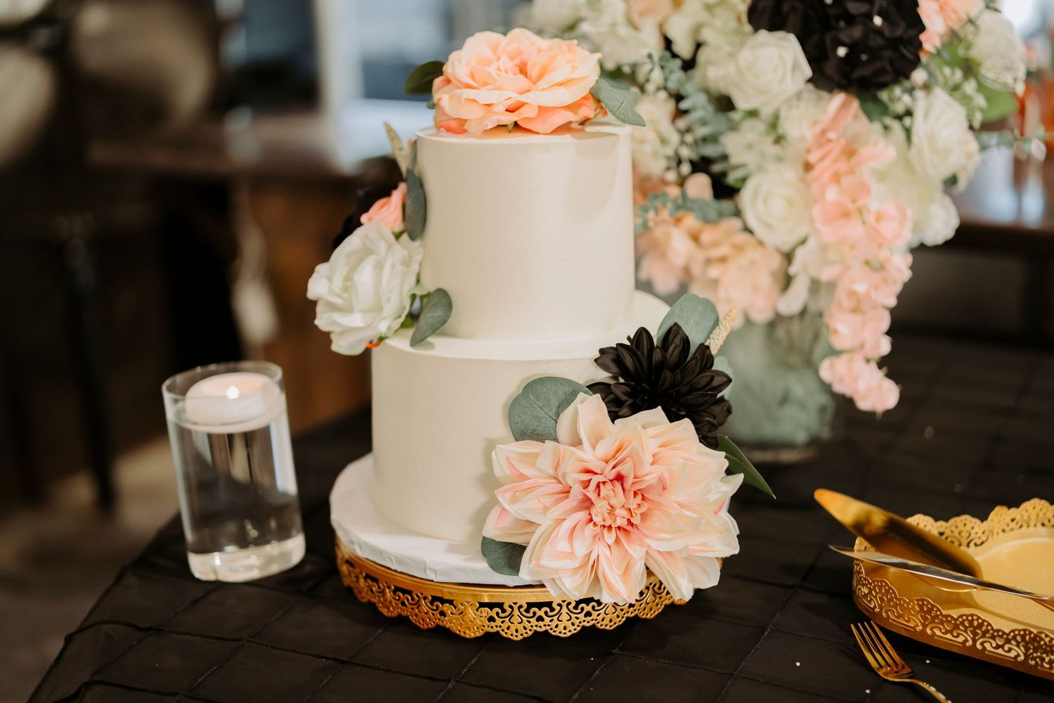 Simple white wedding cake adorned with peach and black flowers displayed on ornate gold base.