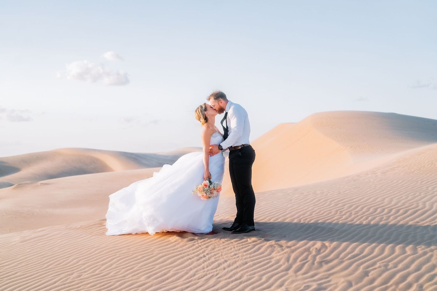 Wedding photos in the desert with a couple sitting gracefully on rolling sand dunes.