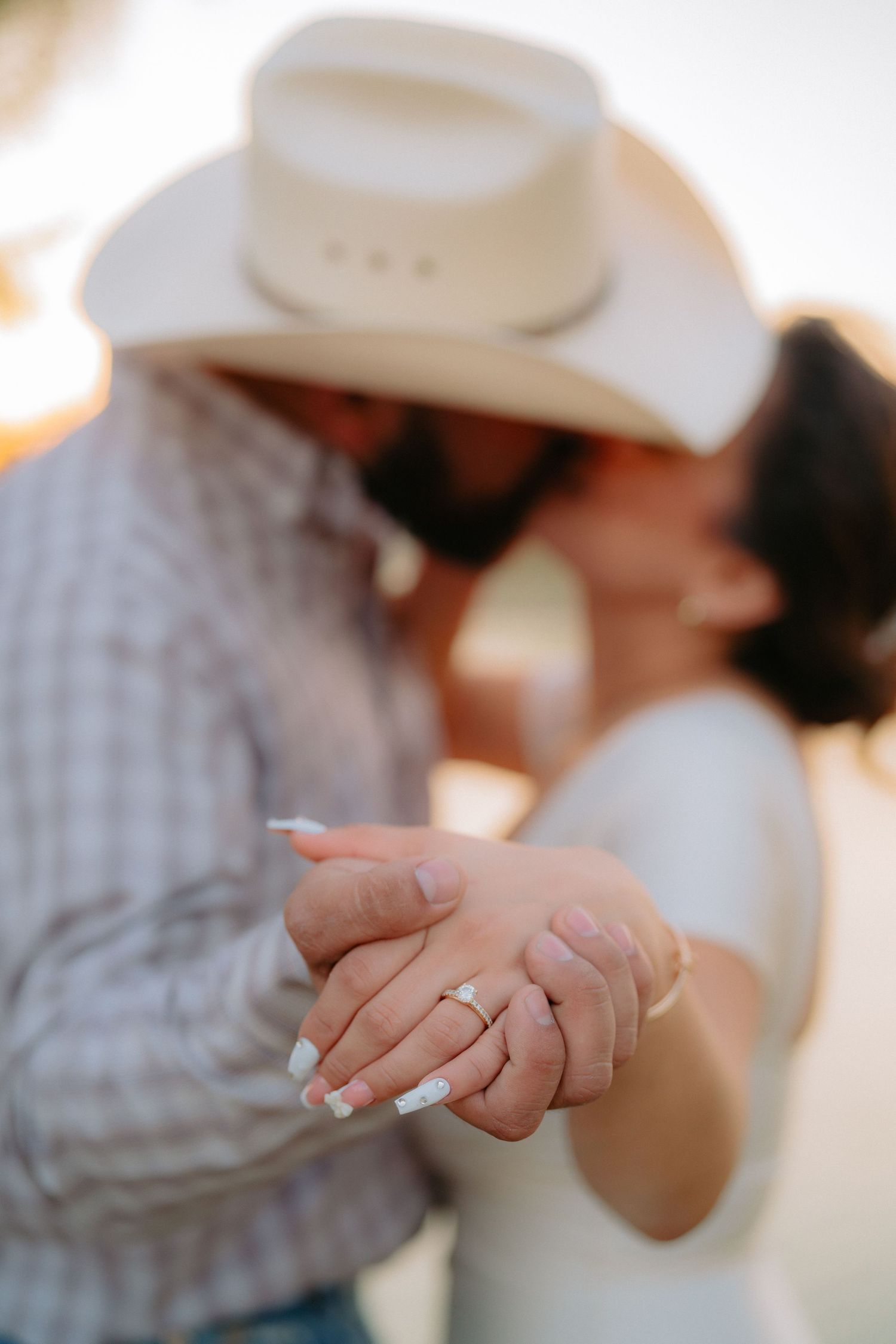 Close-up of couple's hands with engagement ring as they embrace under cowboy hat.