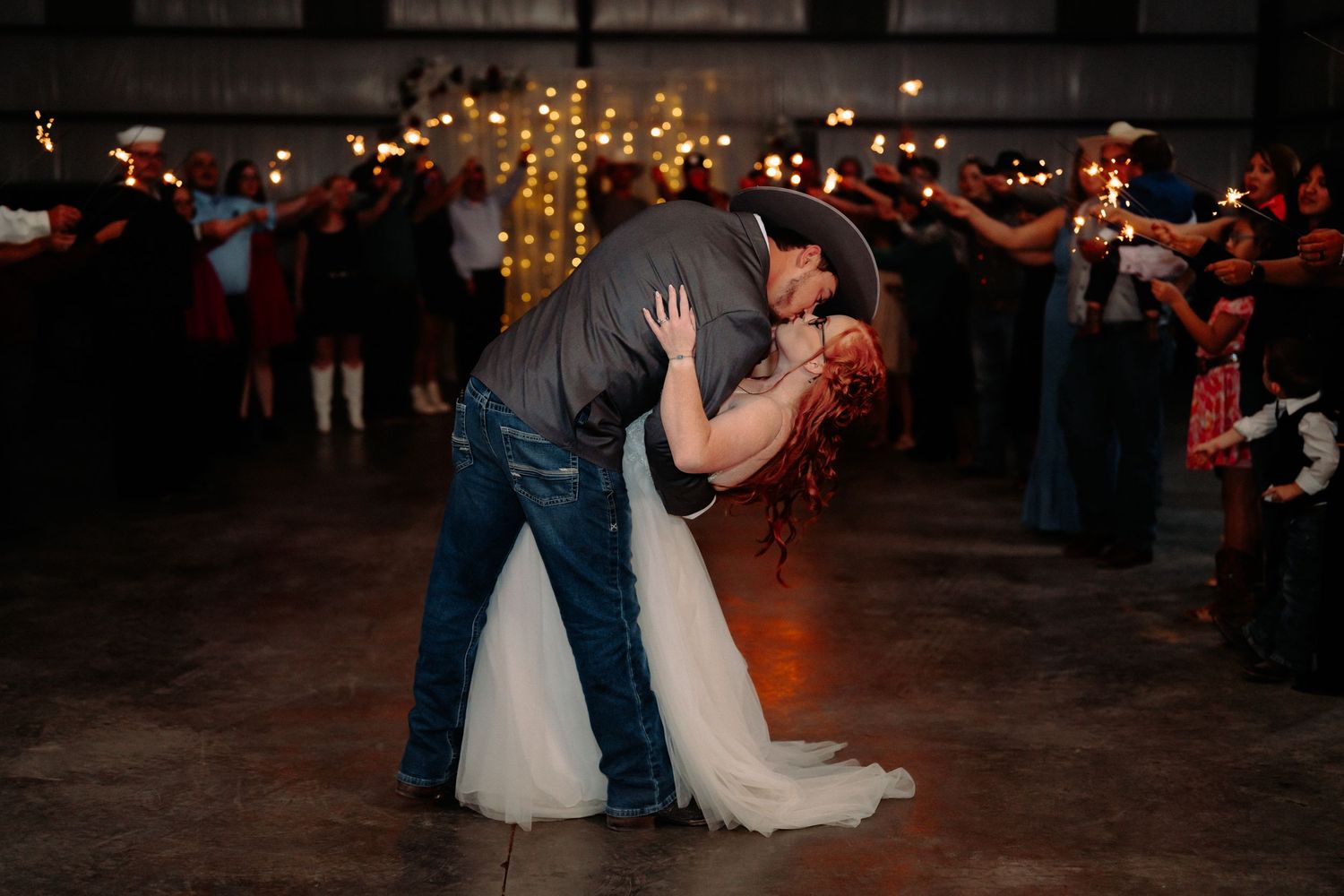 Couple shares a romantic dance dip moment under twinkling lights at their wedding reception.