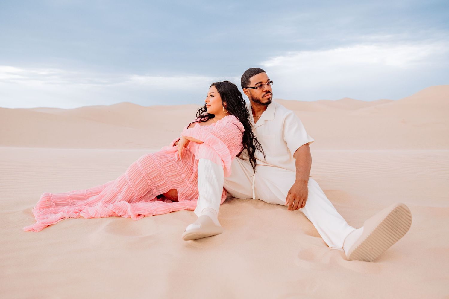 Couple lounging on white sand dunes during romantic desert photoshoot.