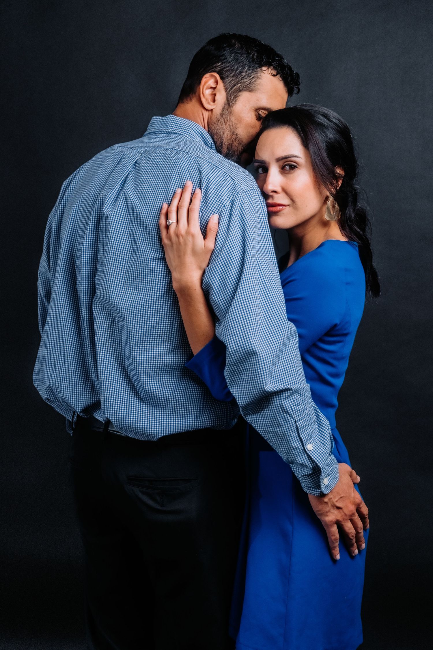 Intimate portrait of couple in coordinating blue outfits against black backdrop.