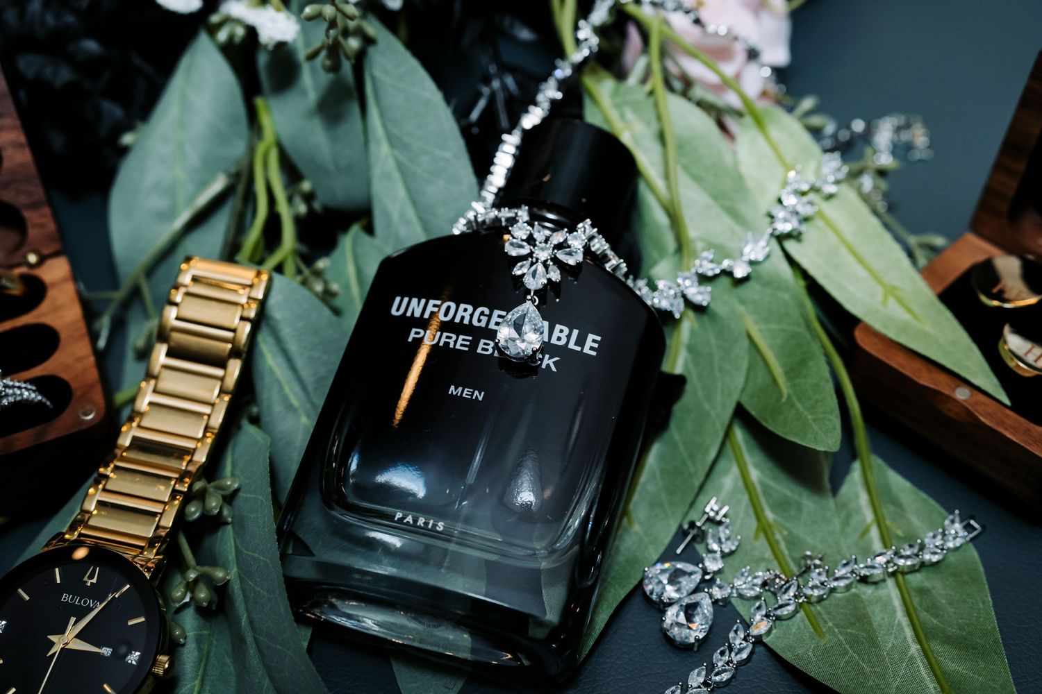 Wedding details with flowers, perfume bottle and gold accessories on dark background.