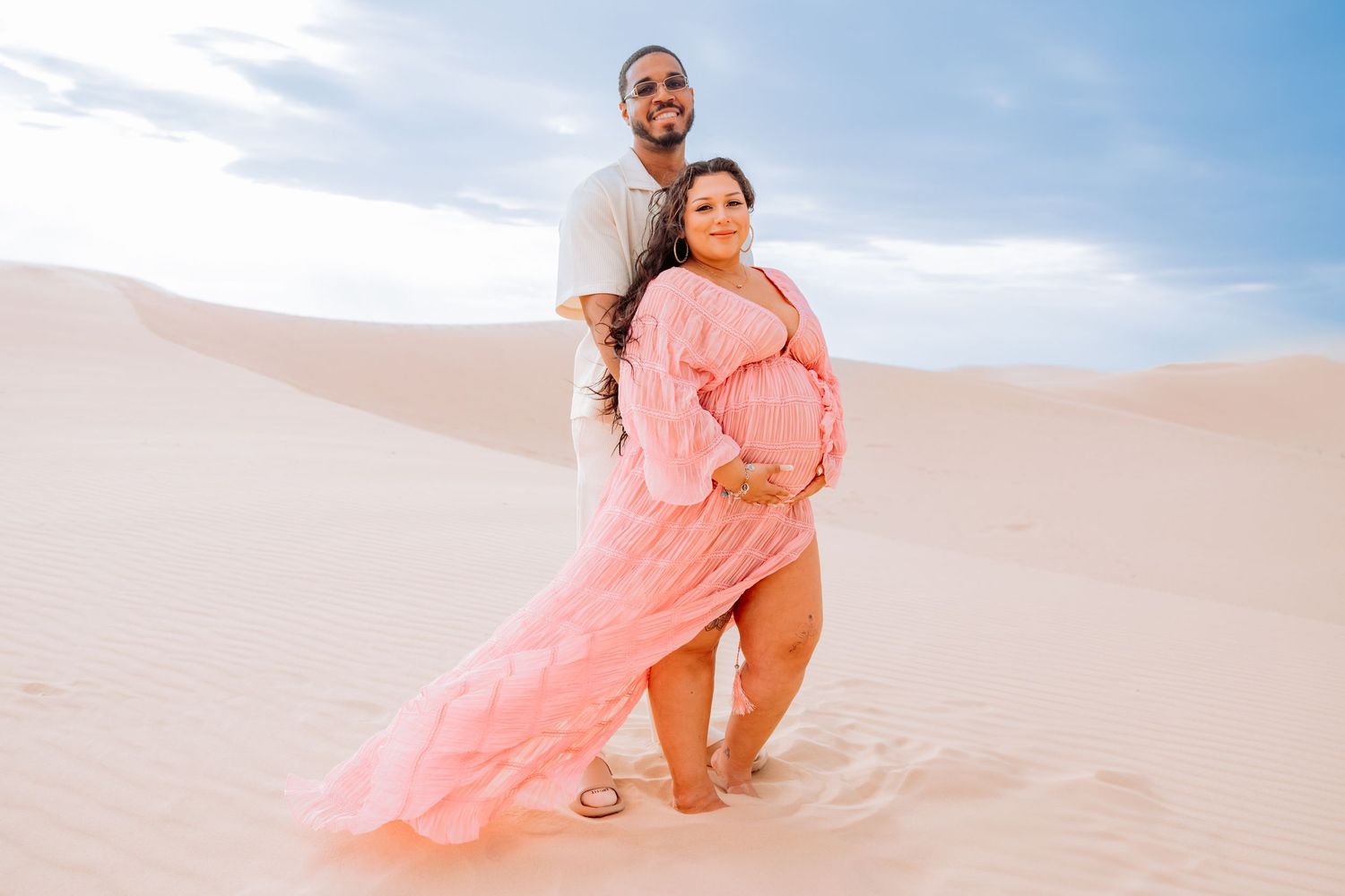 Couple sharing intimate moments during beach photoshoot in white and pink outfits.