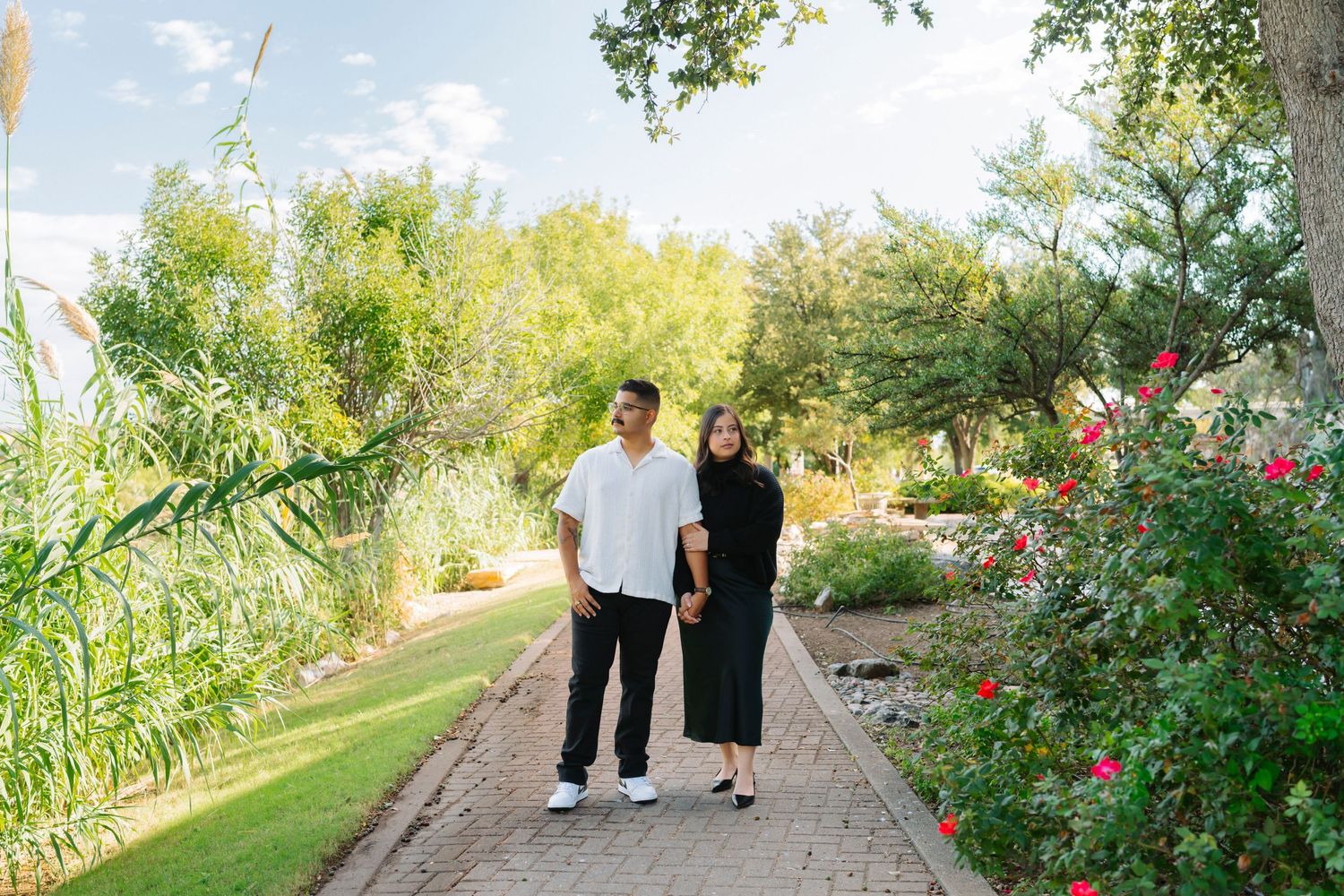People walking along a scenic garden path with blooming flowers and trees on a sunny day.