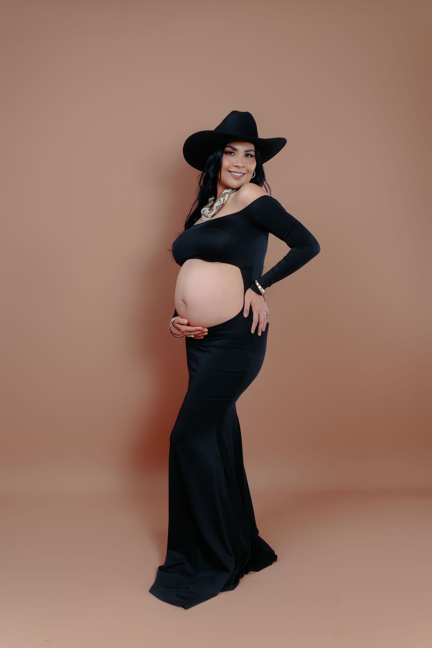 Dramatic maternity photo with woman in flowing black dress and wide-brimmed hat.
