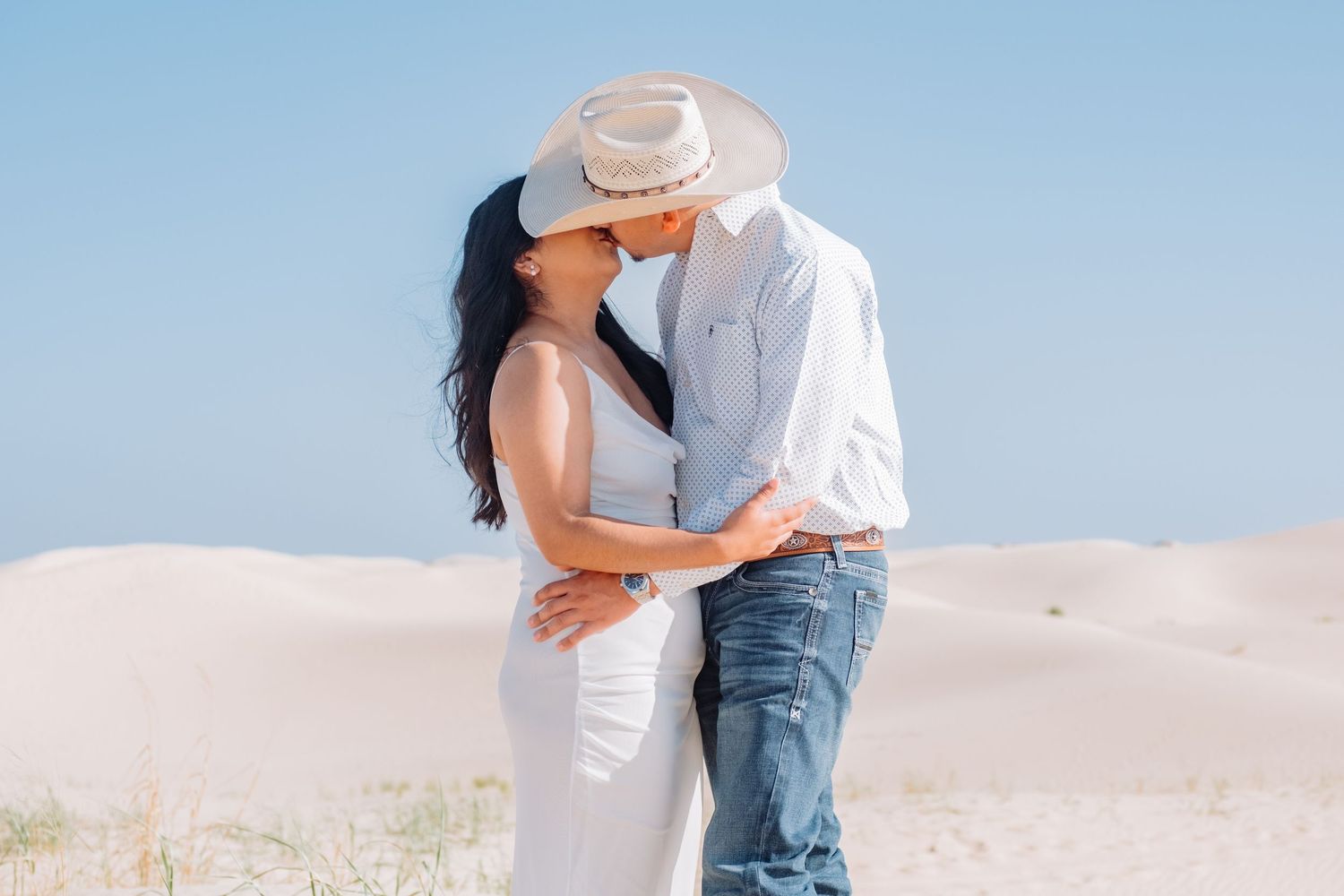 Romantic couple embracing on sand dunes in western-inspired attire.