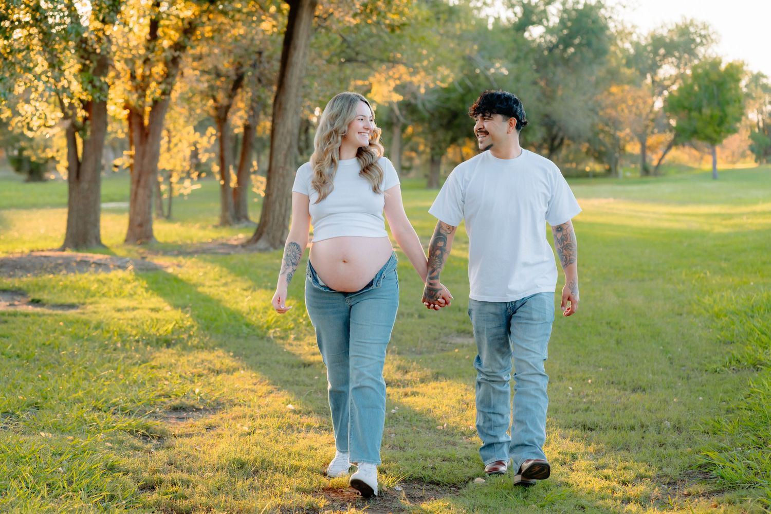 Expectant couple walking together during golden hour photo session in a park.