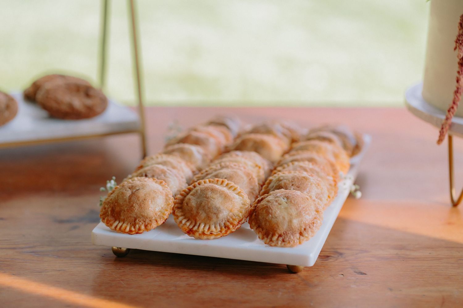 Row of golden brown pastry empanadas lined up on a white serving platter at a wedding reception.