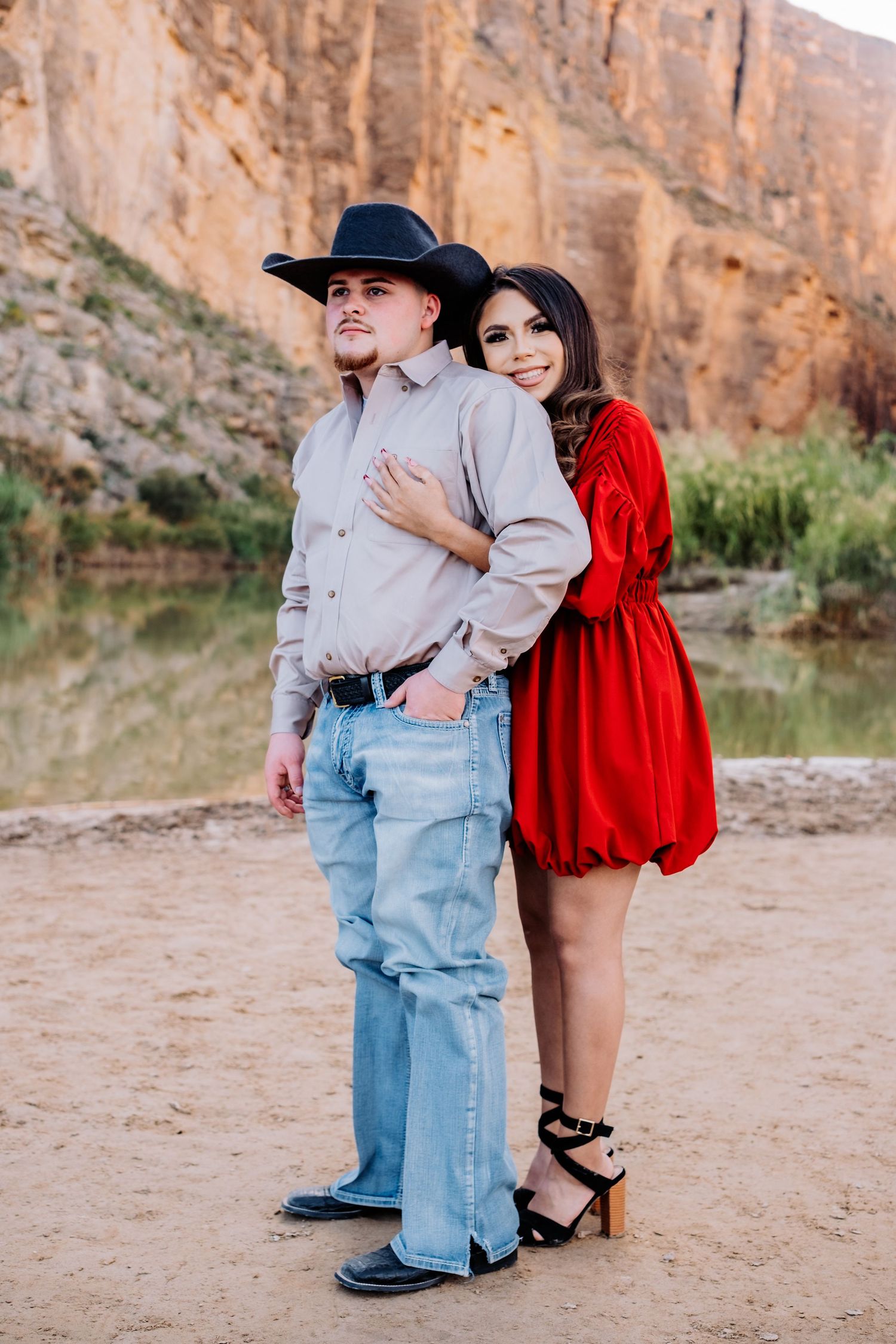 Couple in contrasting western outfits pose together near scenic canyon walls.