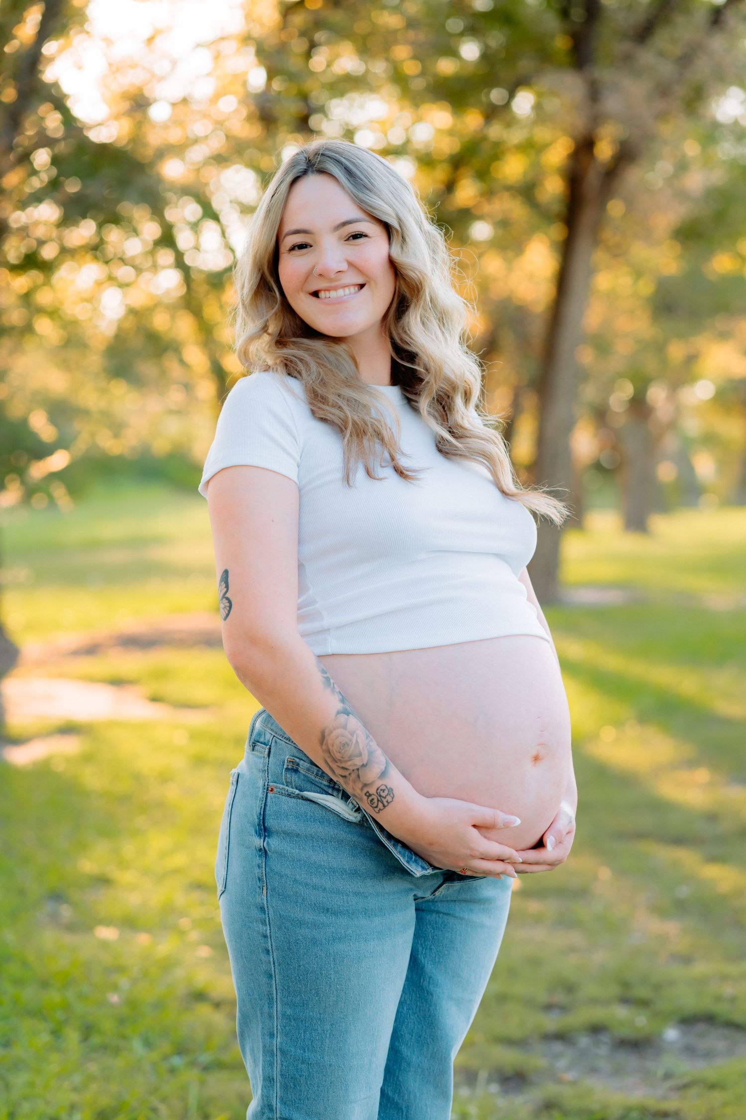 Expecting mother poses in jeans and white top during golden hour photography session.