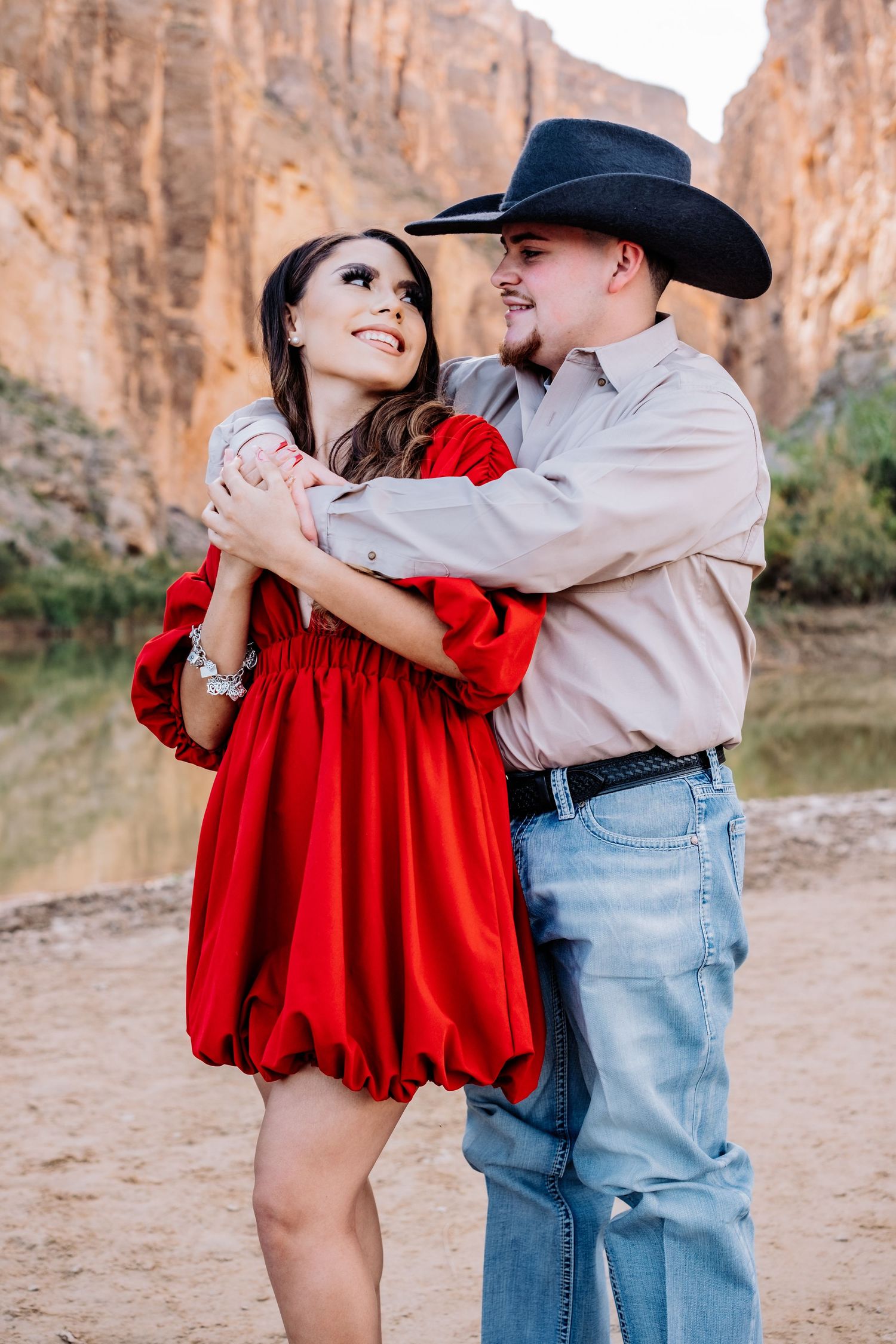 Happy couple sharing playful moment in western attire against desert canyon backdrop.