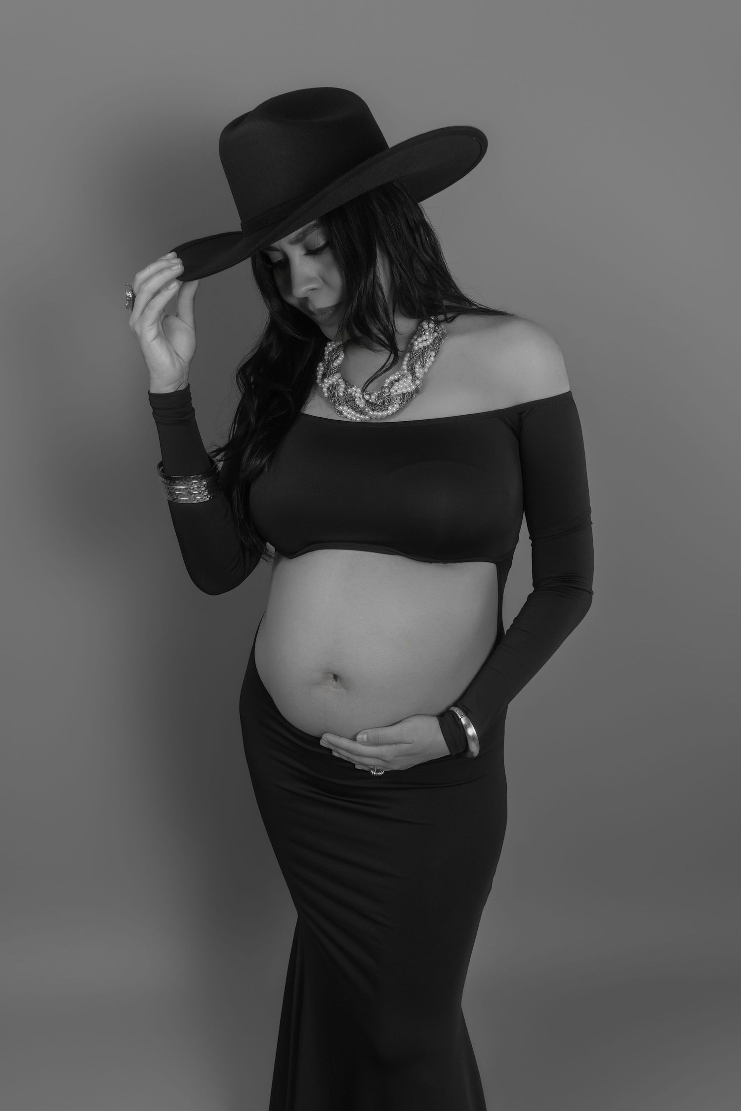 Stylish maternity photos featuring black attire and a wide-brimmed hat against gray background.