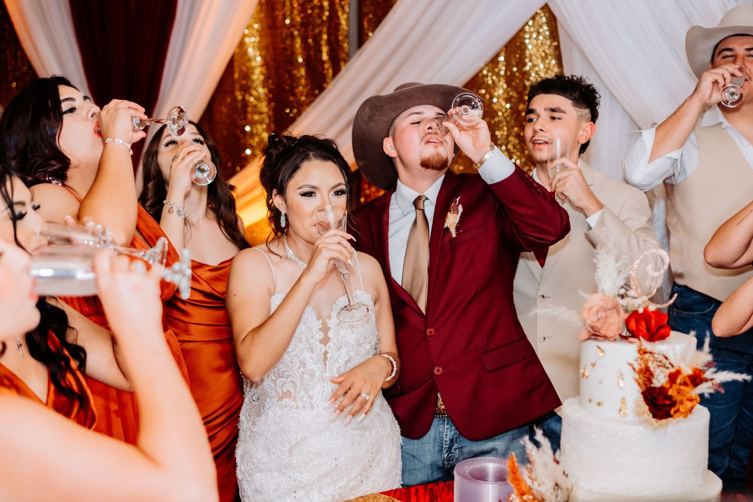 Wedding celebration with guests dancing and enjoying festivities against gold sequin backdrop.