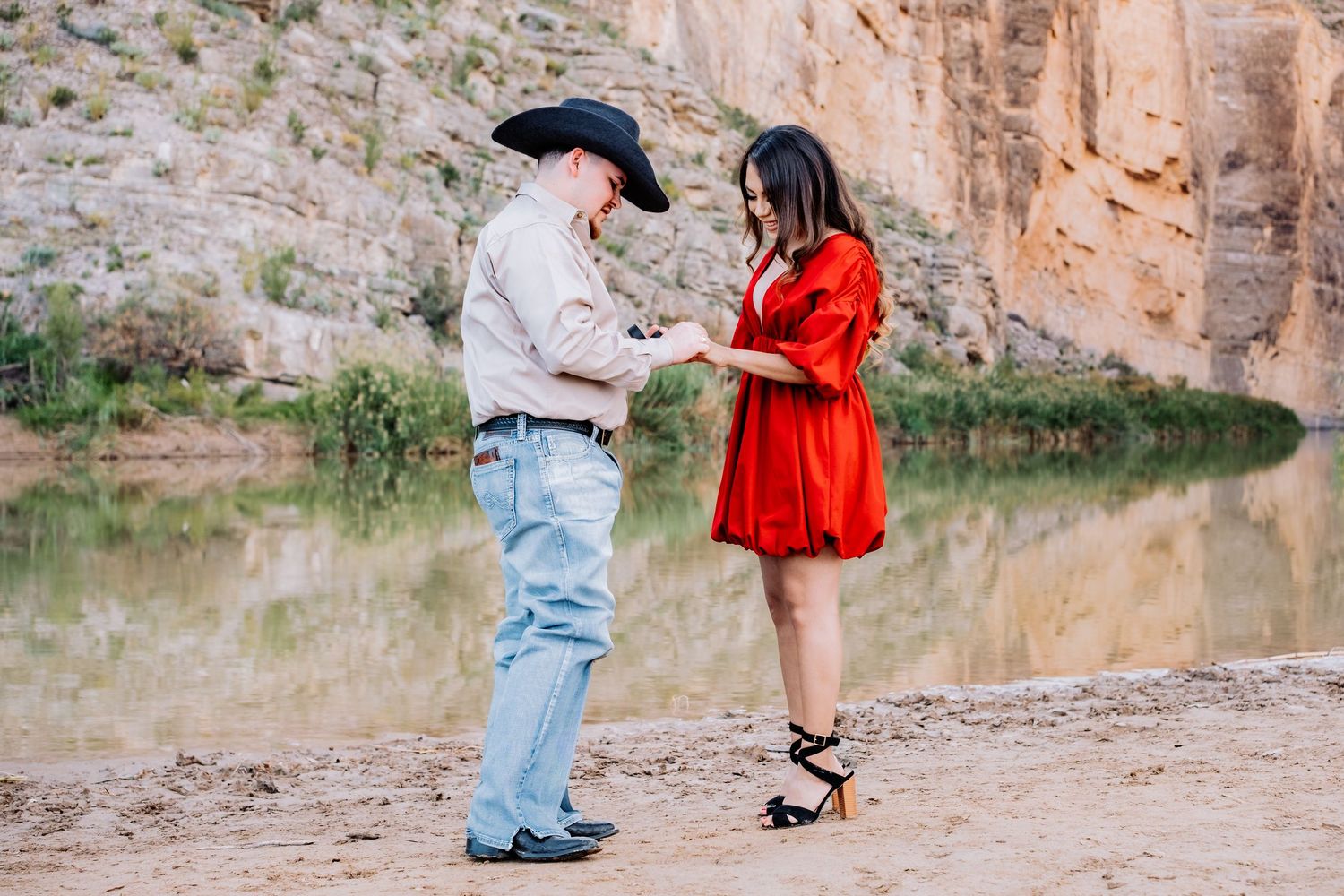 Couple in casual western attire sharing a romantic moment near canyon cliffs and water.