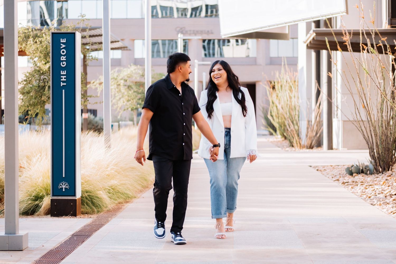 Two people walking and interacting along a modern urban pathway with buildings nearby.