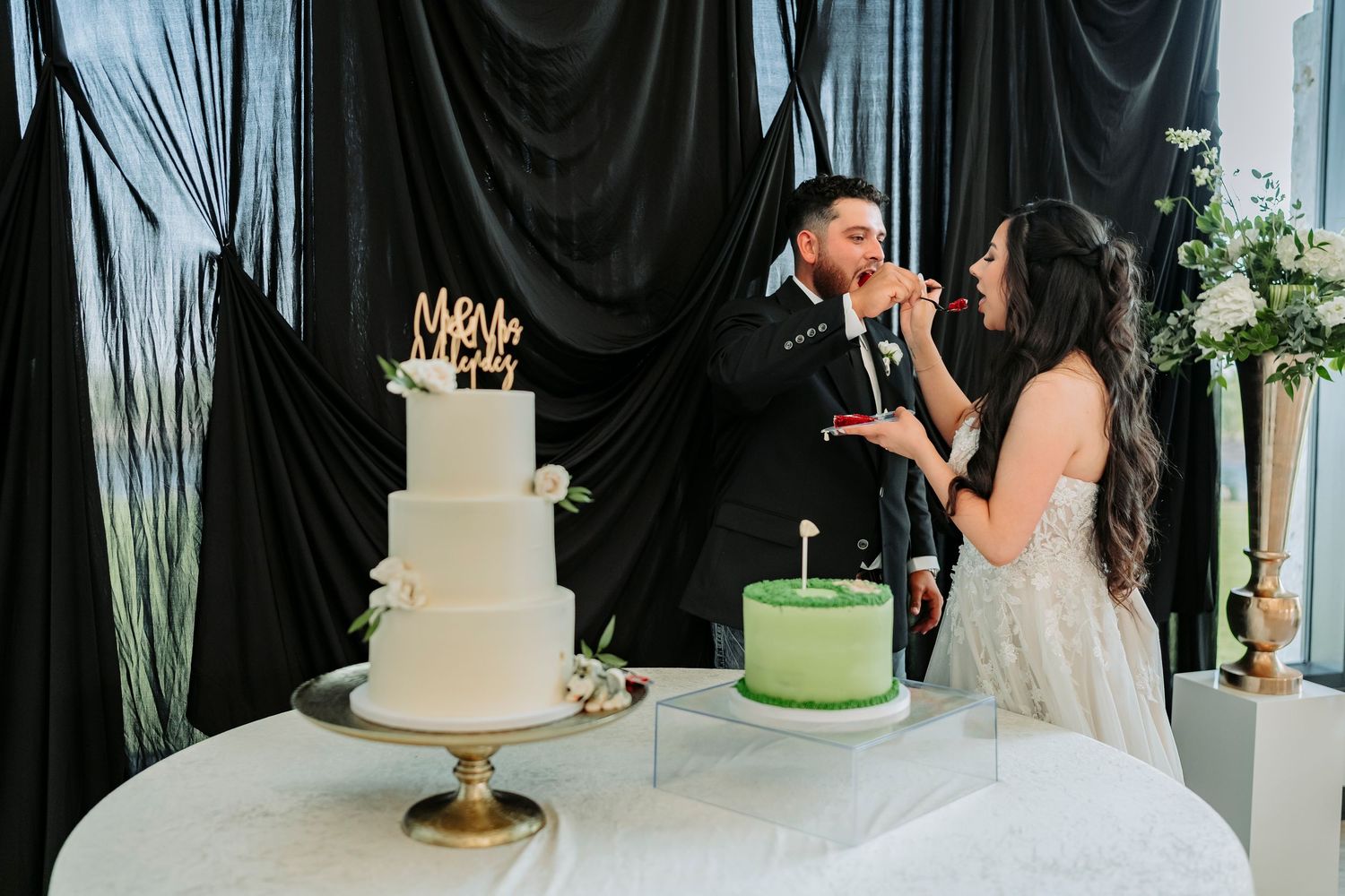 Wedding cake display setup with black backdrop and greenery decorations at an elegant reception.