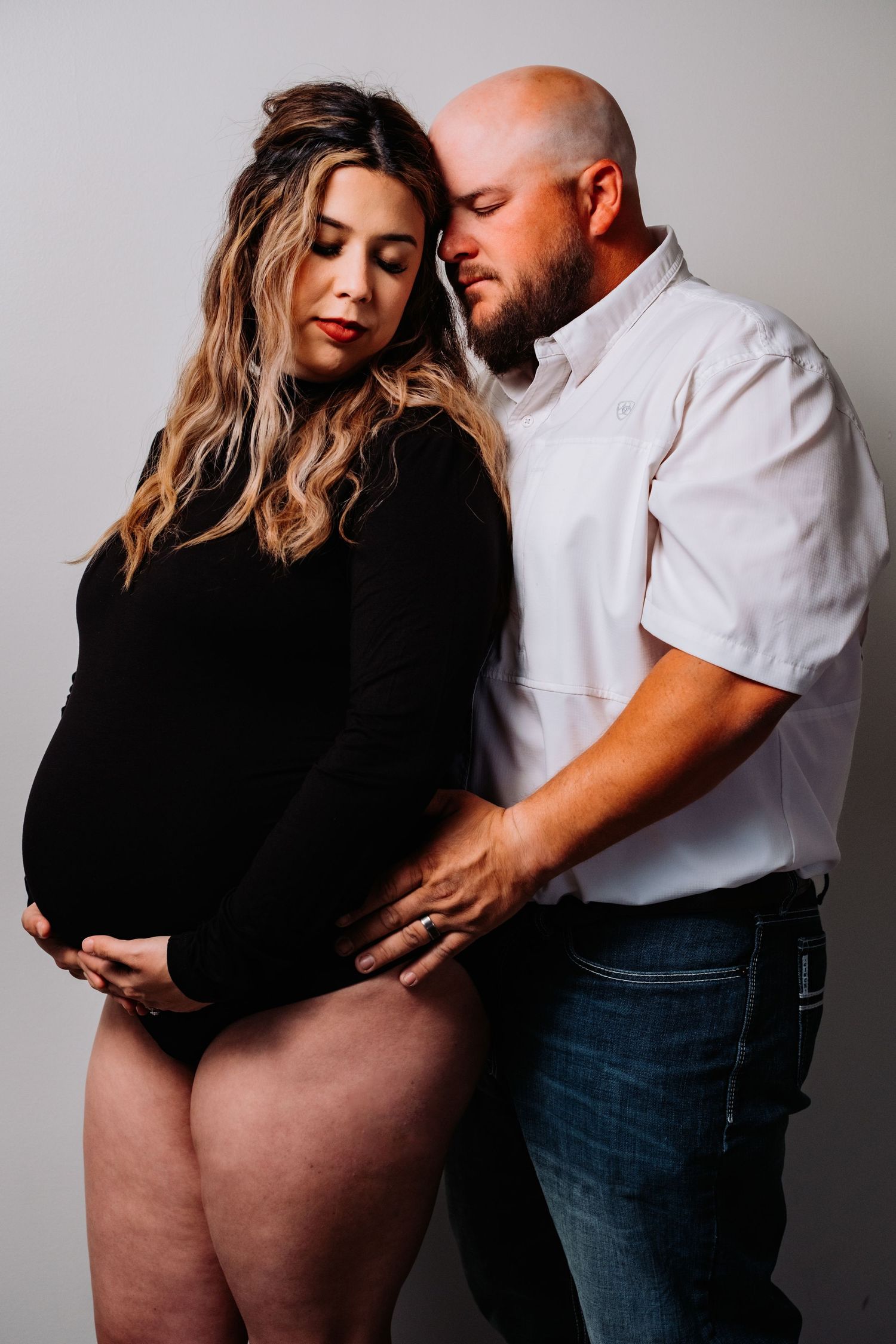 Studio maternity portrait featuring couple in black and white clothing.