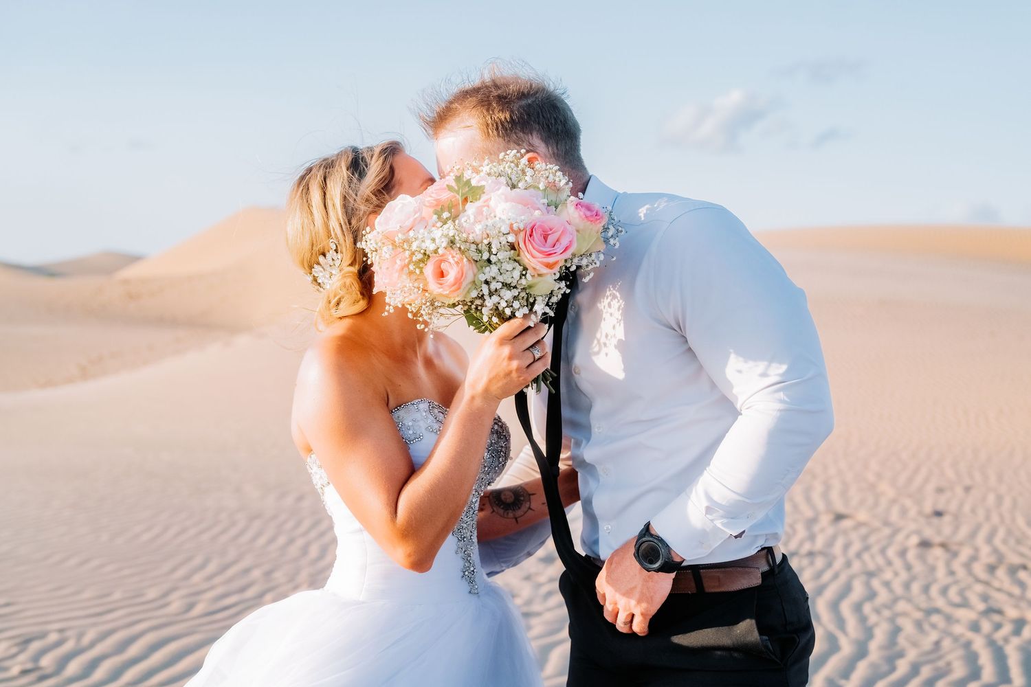 Scenic desert engagement photoshoot with a couple posing against rippled sand dunes at sunset.