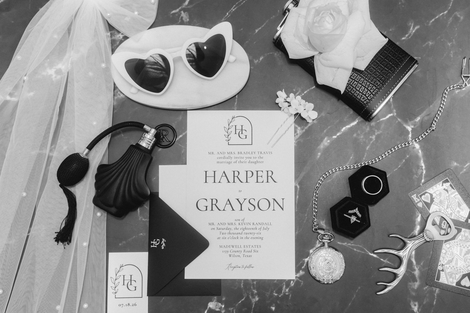 Wedding stationery and accessories arranged in a monochromatic flat lay style.
