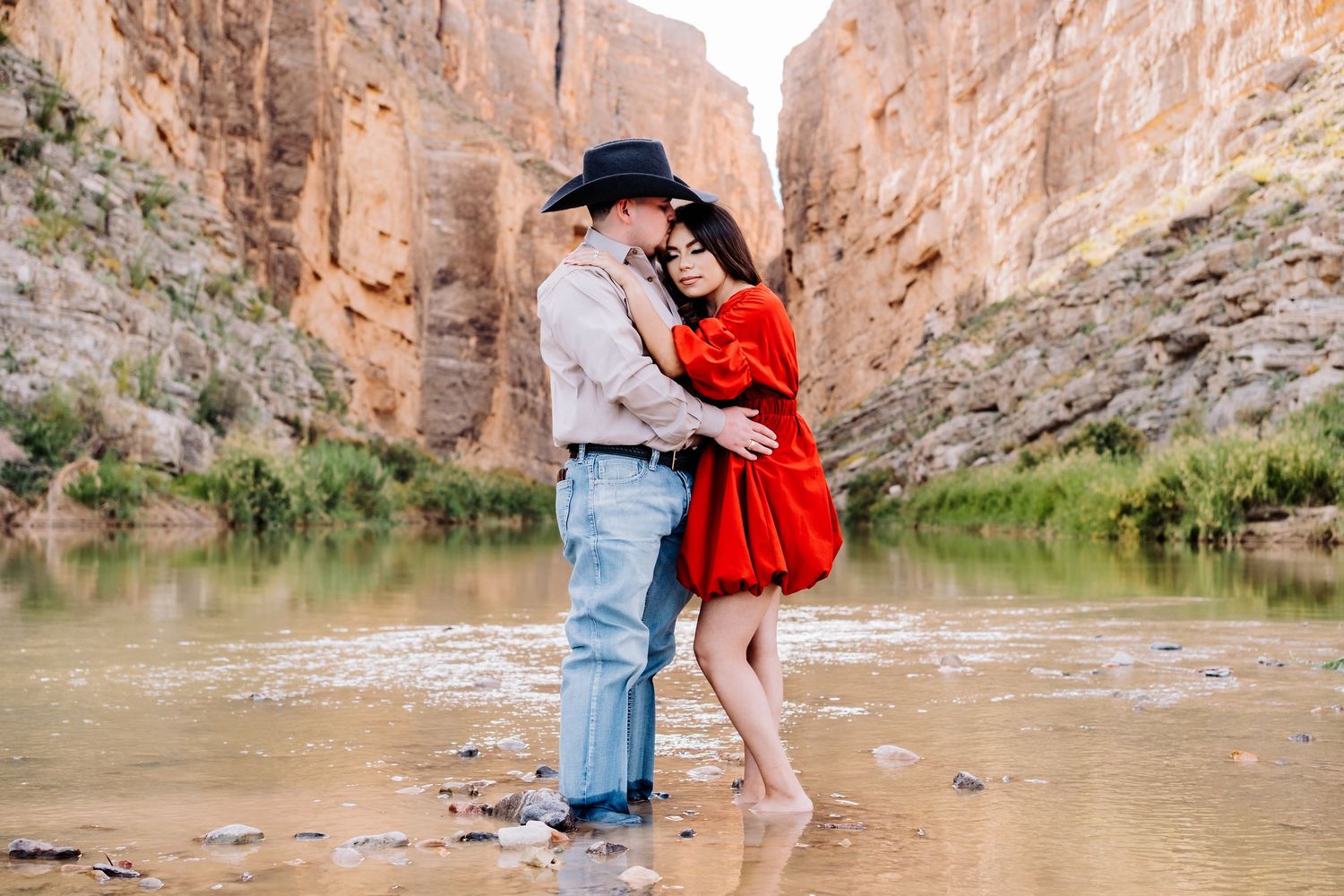 Romantic couple embrace while standing in water, surrounded by towering canyon walls.