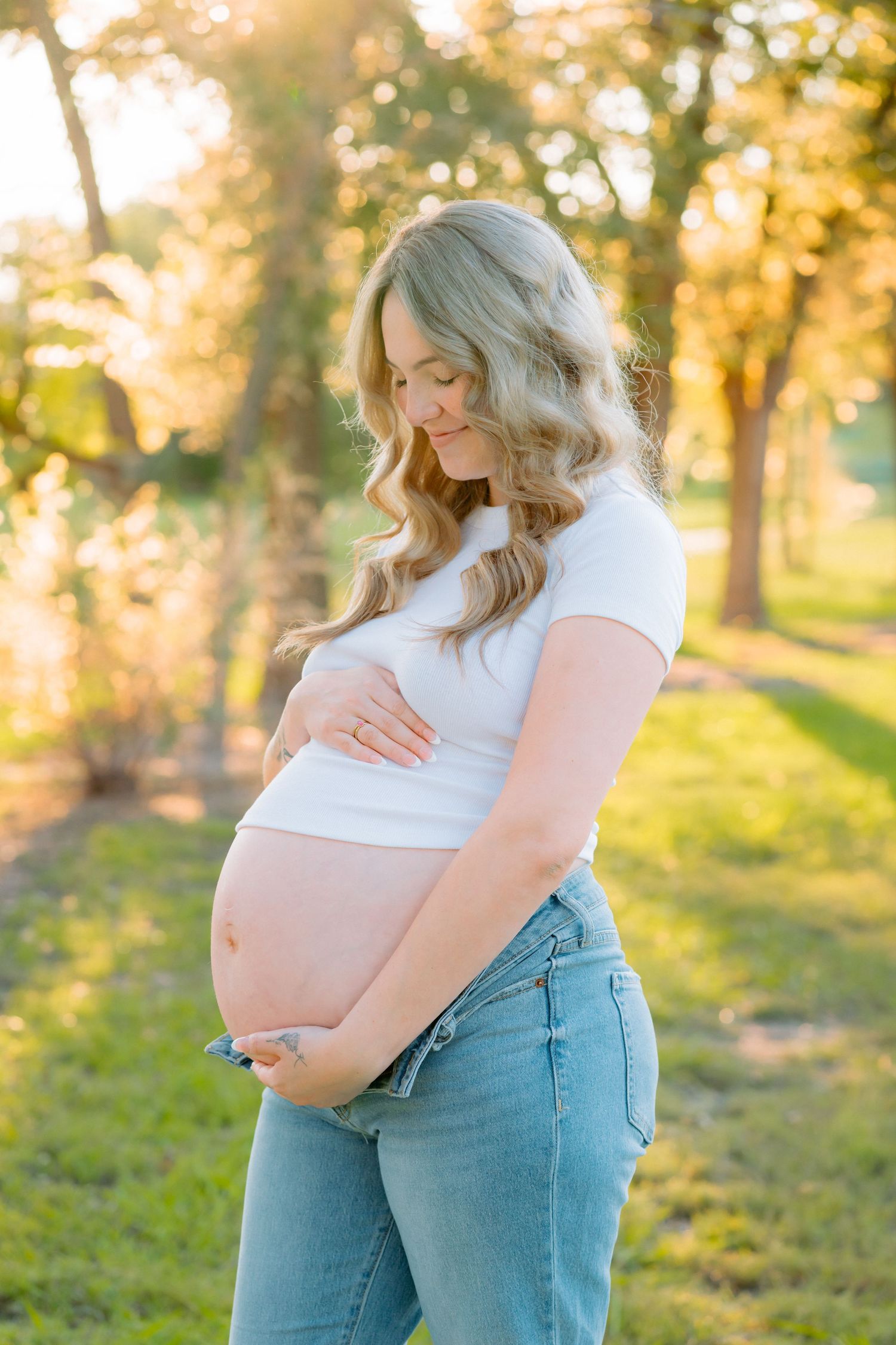 Maternity photoshoot in a sunlit park showing a closeup of an expectant mother's baby bump.