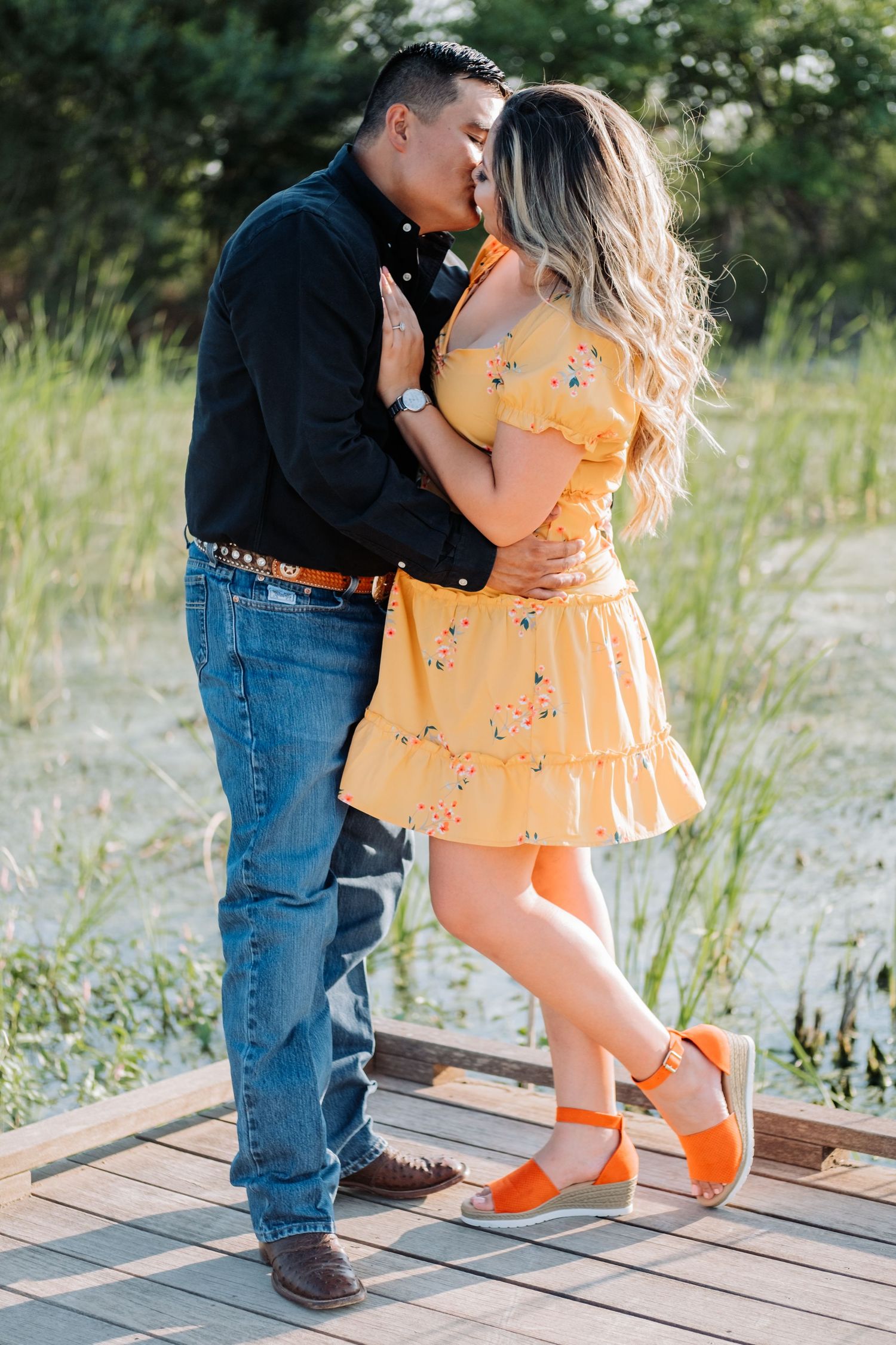 Couple in casual wear sharing romantic moment on wooden deck surrounded by grass.