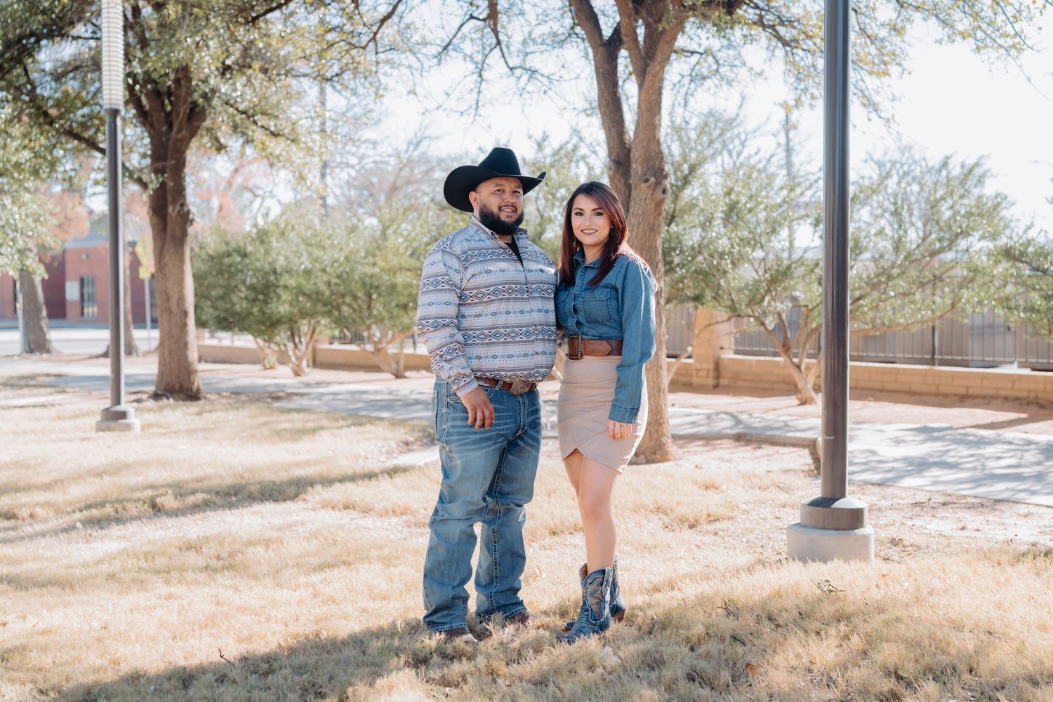 Couple in western-themed outfits shares candid moments during outdoor session.
