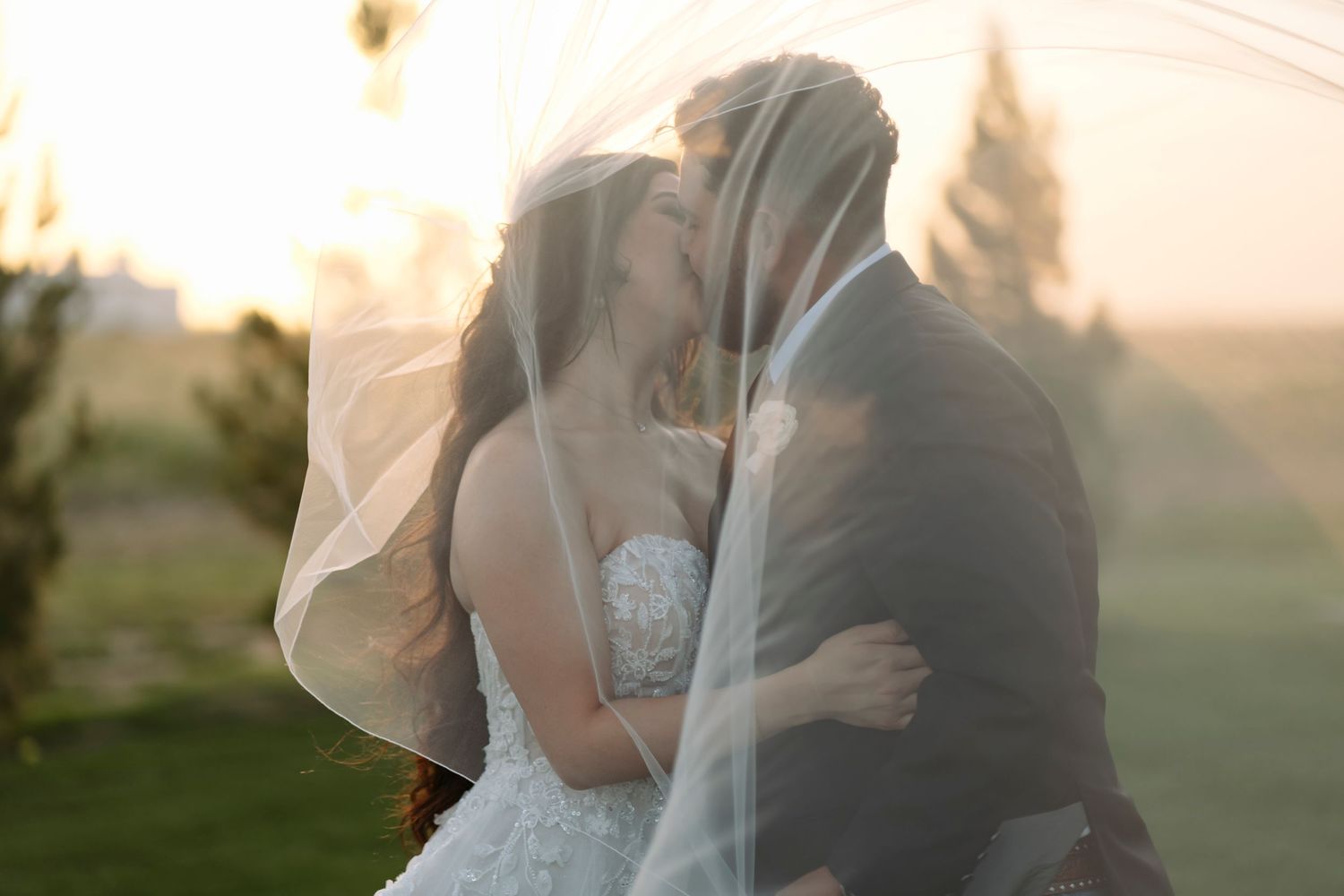 A couple in wedding attire embraces during golden hour in a scenic outdoor setting.