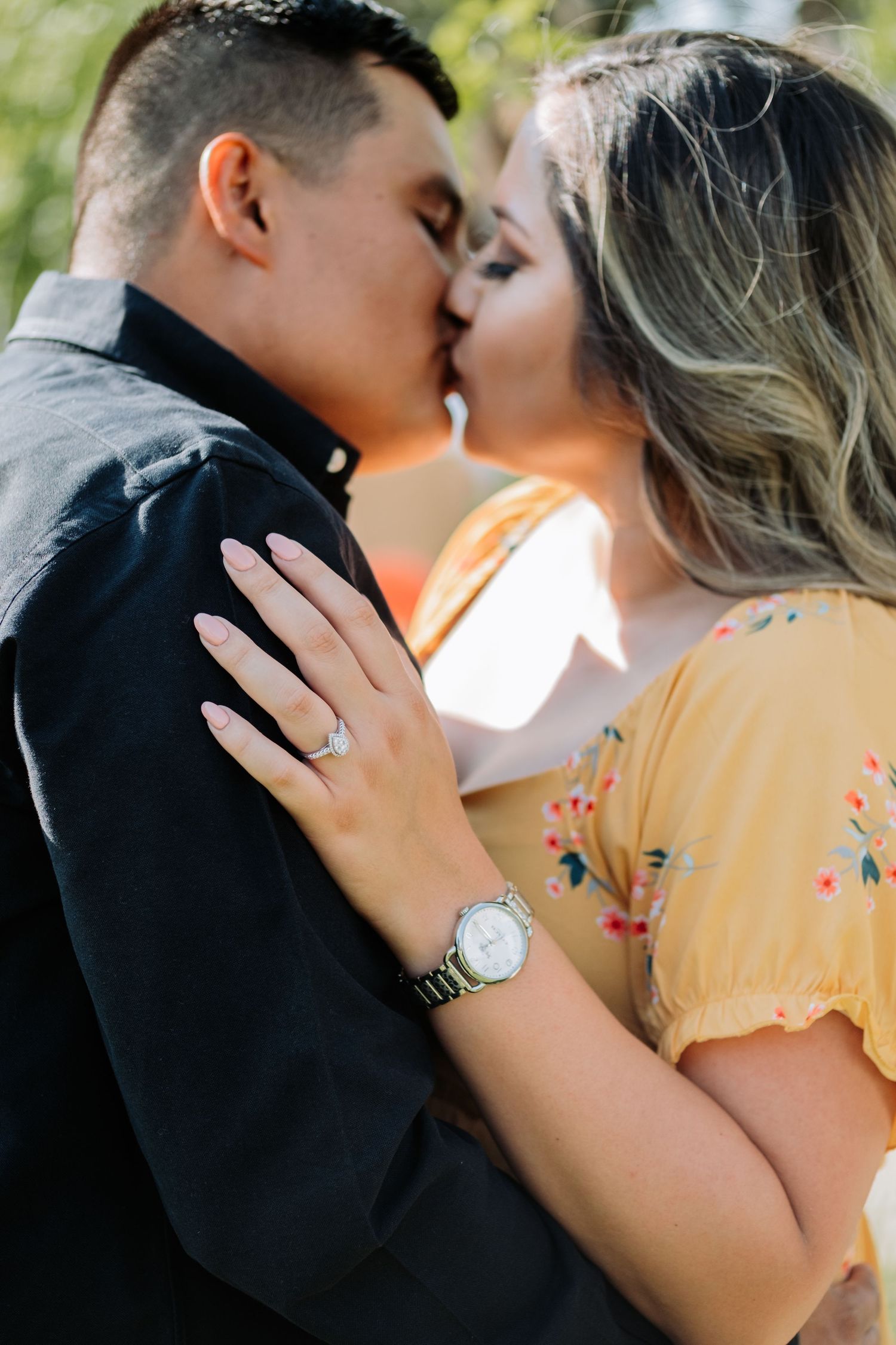 Intimate engagement photo of couple kissing, with woman's ring visible on her hand.