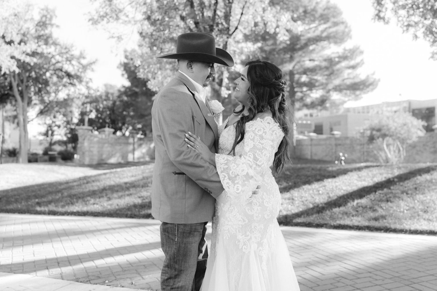 Bride in lace dress and groom in cowboy hat share intimate outdoor moment on their wedding day.