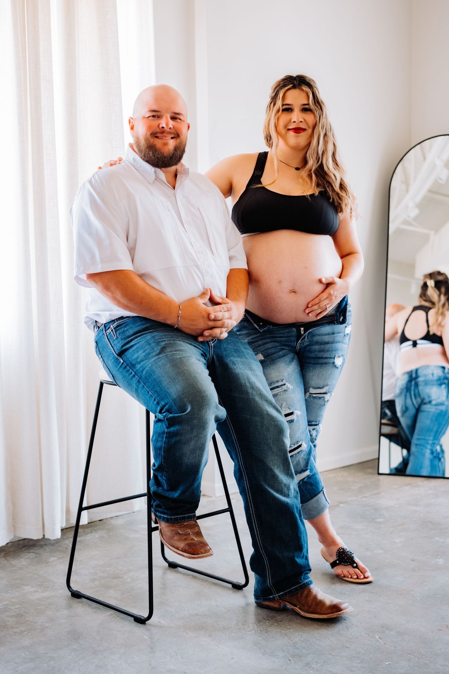 A maternity photoshoot featuring casual attire and intimate poses against a light backdrop.