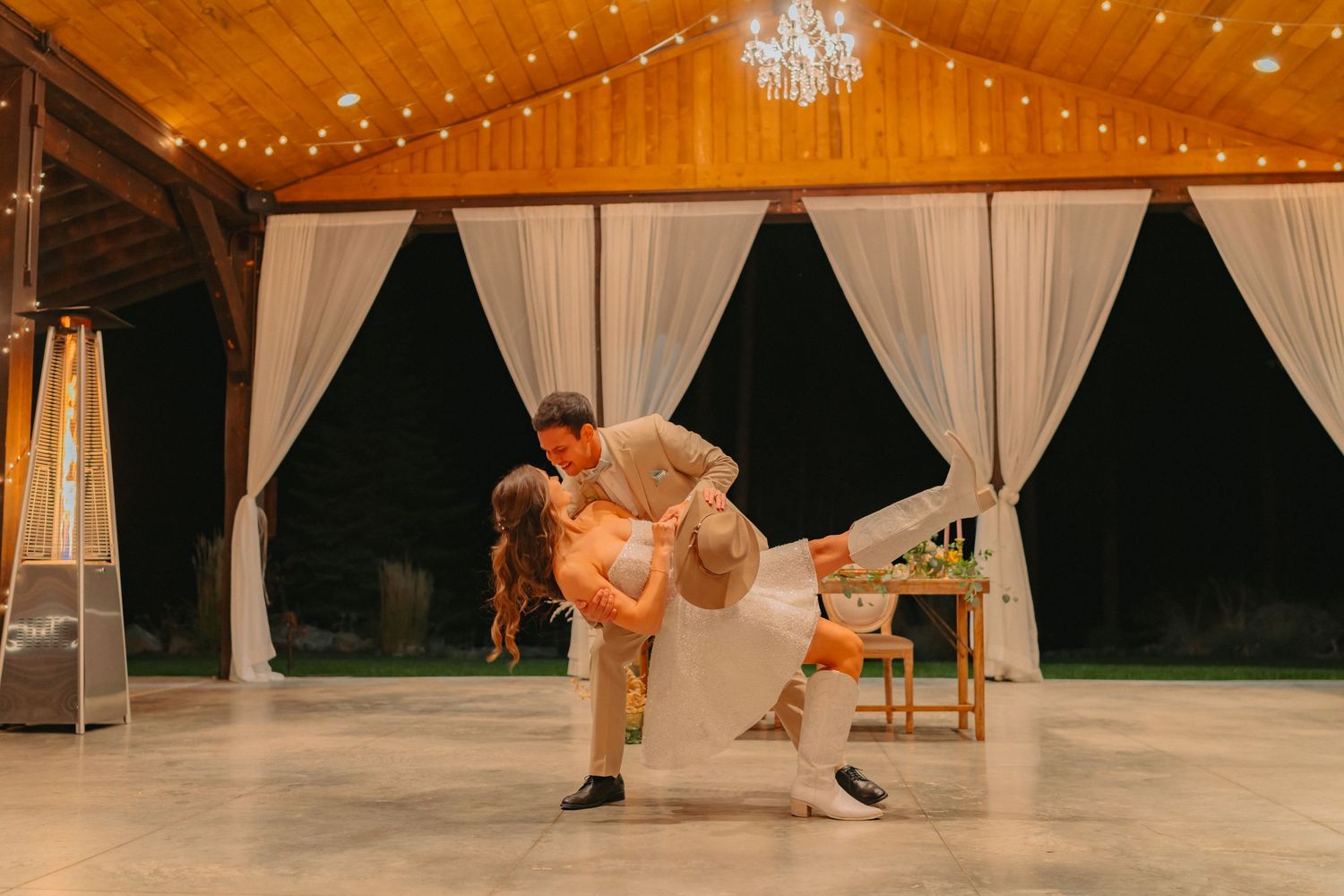 A romantic wedding dance dip under twinkling lights in a rustic barn venue.