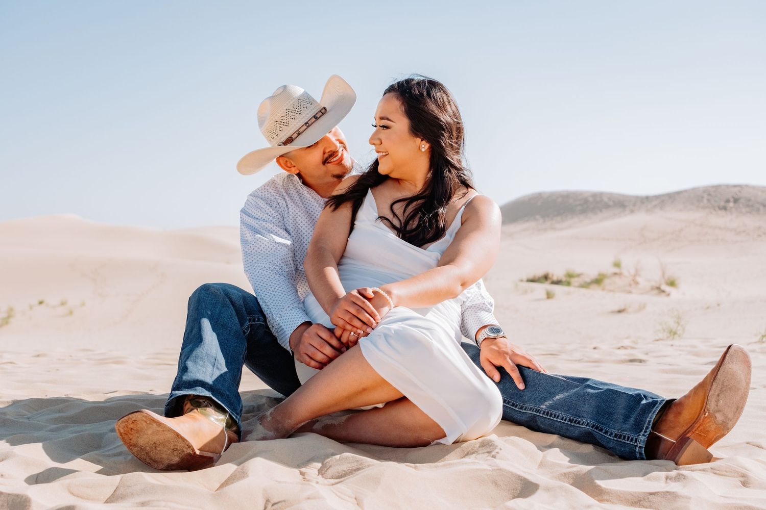 Couple sitting casually on sand dunes sharing a laugh together.