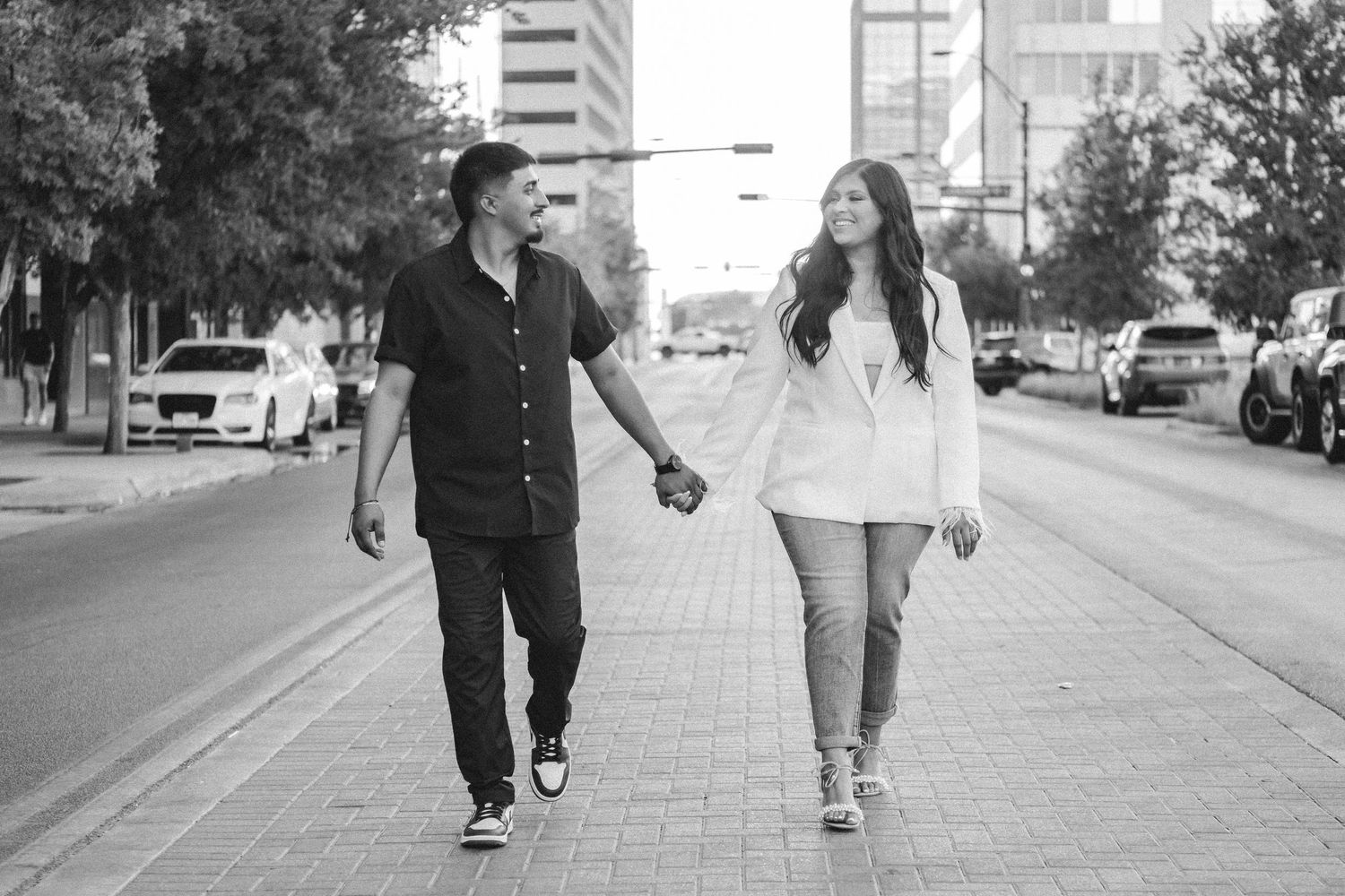 Two people walking together on an urban sidewalk with buildings in the background.